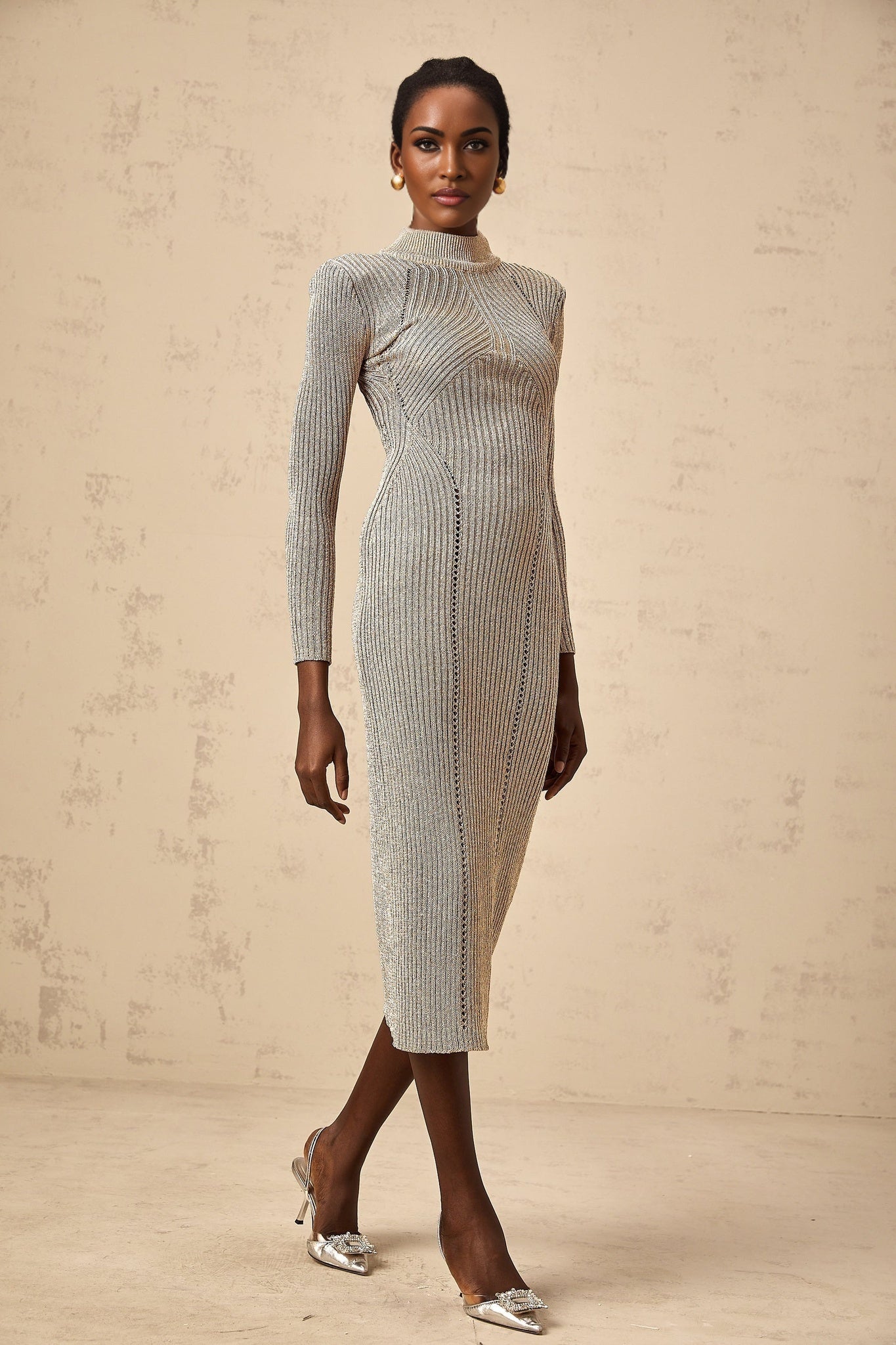 A gold colored midi dress with a ribbed knit texture and delicate pointelle pattern details worn by a model standing in a neutral setting