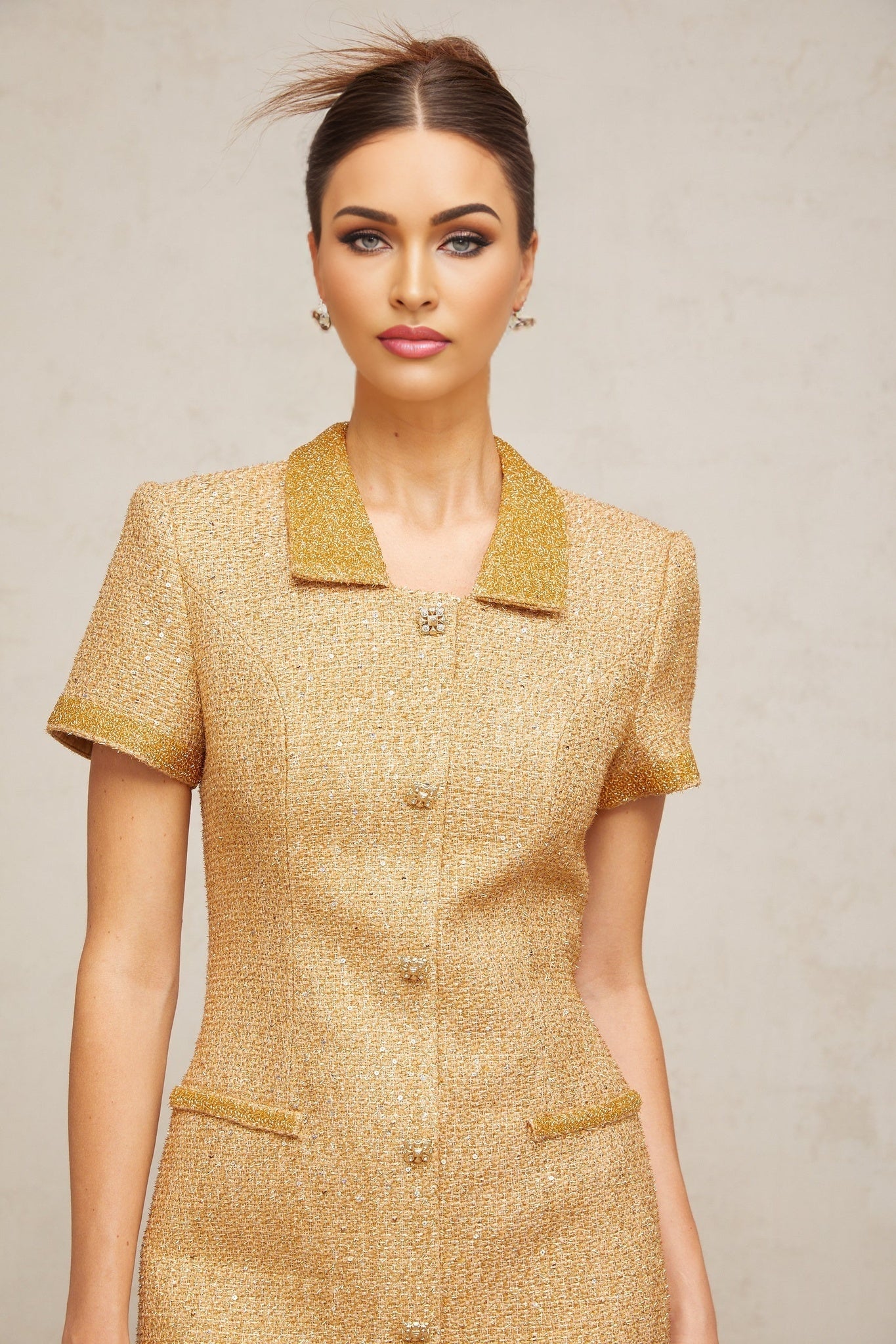 A gold sequined tweed mini dress with a sleeveless design and short hemline featuring a shimmering textured fabric