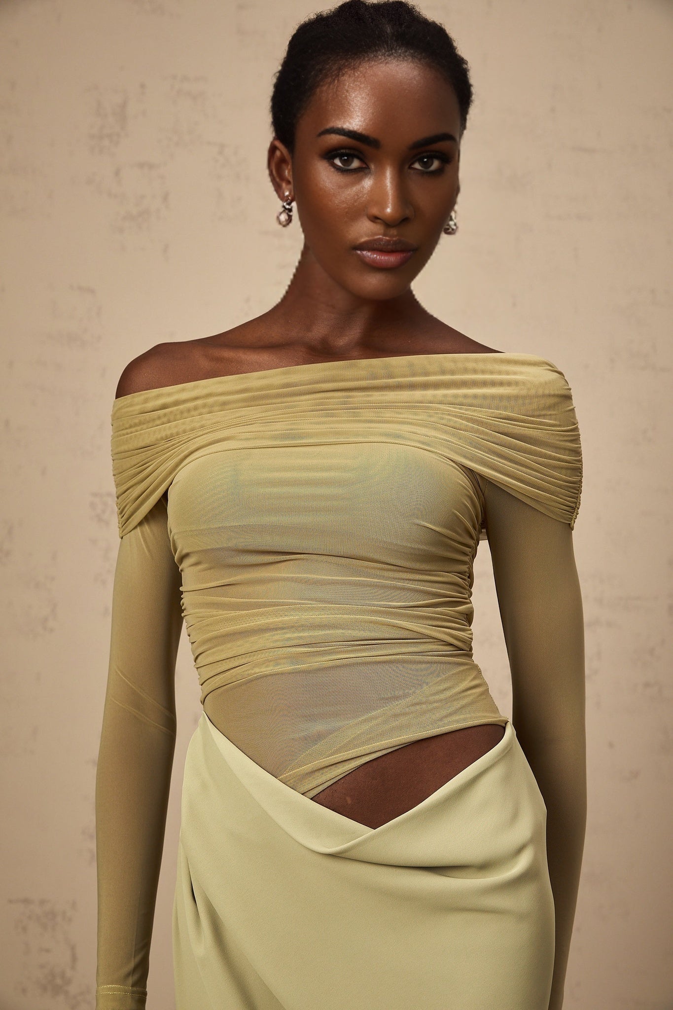 A green offshoulder midi dress with a semisheer fabric and a flowing silhouette worn by a model against a plain background