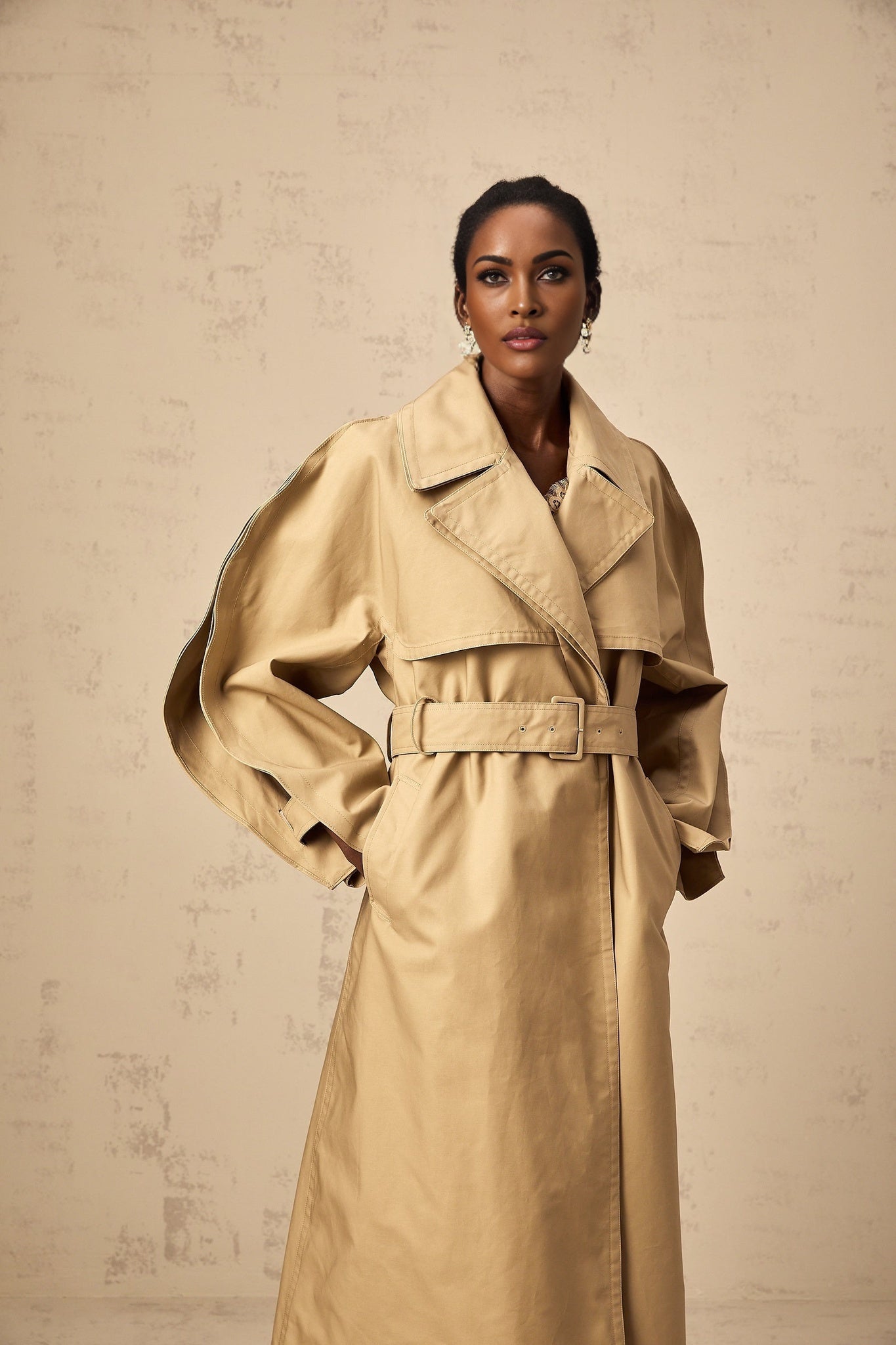 A khaki trench coat with curved sleeves modeled by a person named Jaden