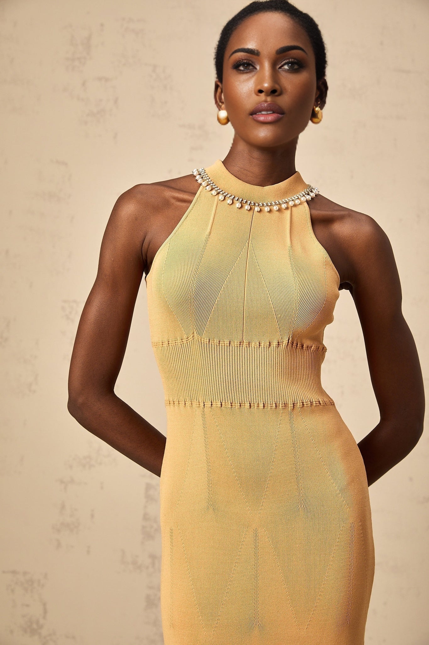 A knit midi dress in a light color with faux pearl embellishments adorning the neckline and sleeves named Juliette