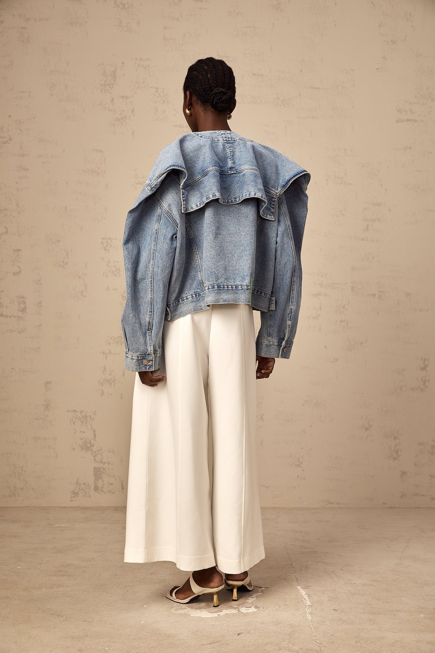 A light blue denim jacket without a collar worn by a model against a plain background