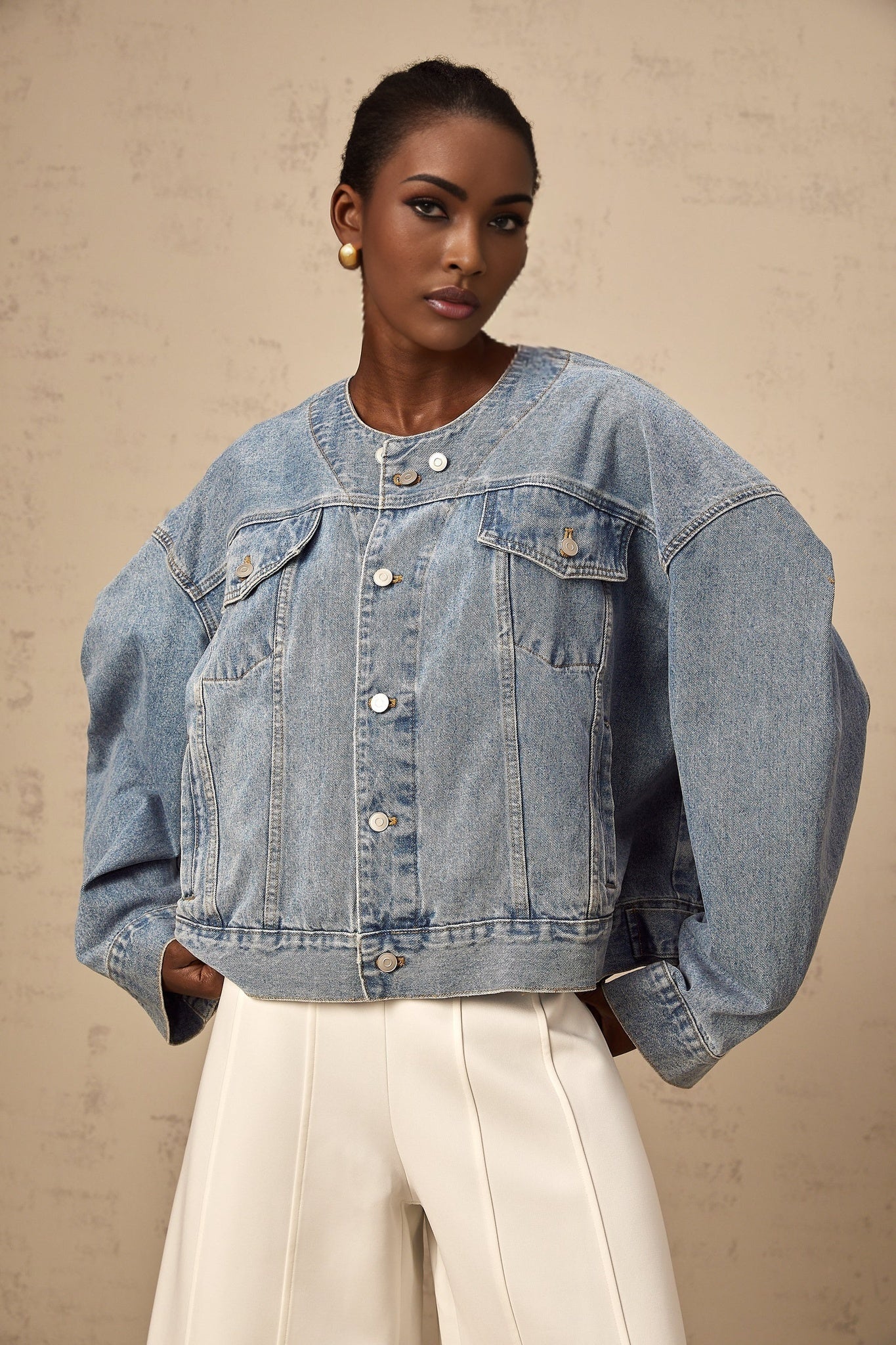 A light blue denim jacket without a collar worn by a woman against a plain background