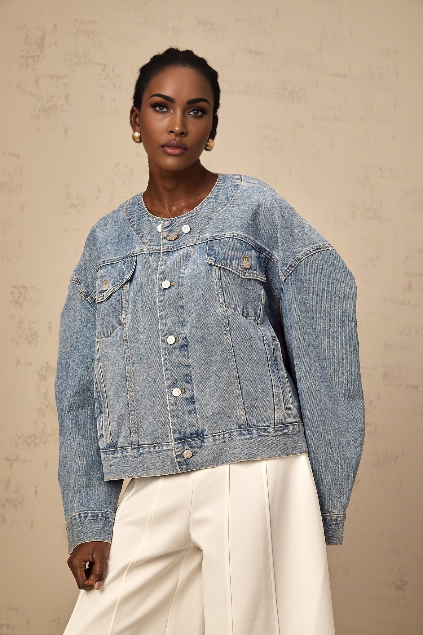 A light blue denim jacket without a collar worn by a woman against a plain background