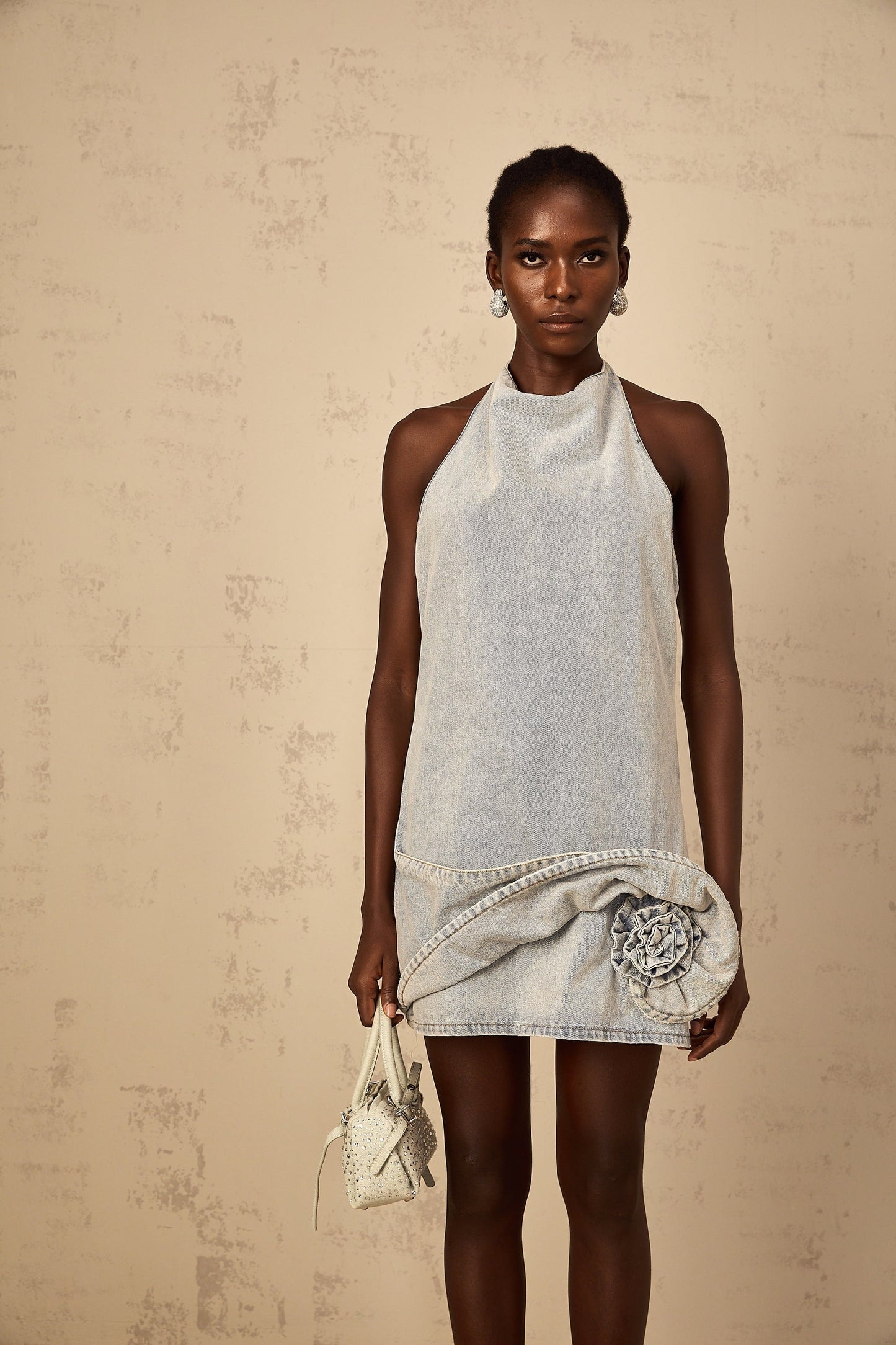 A light blue denim mini dress with a halterneck style featuring a fitted silhouette and short hemline