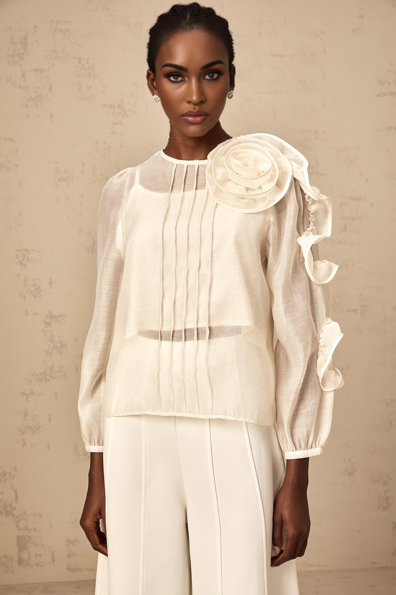 A light colored blouse with three dimensional floral details and a semi sheer fabric