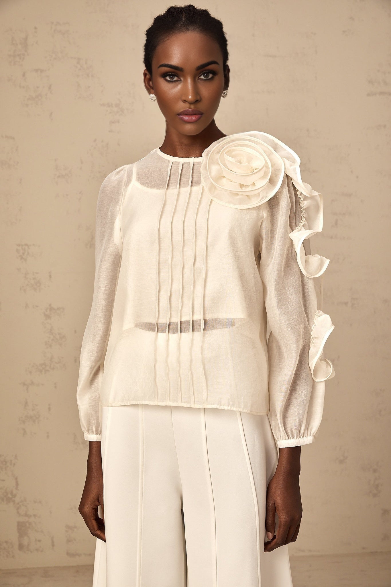 A light colored sheer blouse with delicate three dimensional floral embellishments scattered across the fabric