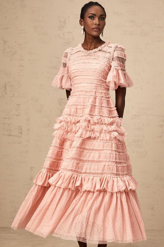 A light pink midi dress with ruffled tulle layers and small dot details throughout the fabric The dress features a feminine silhouette with a fitted bodice and flowing skirt
