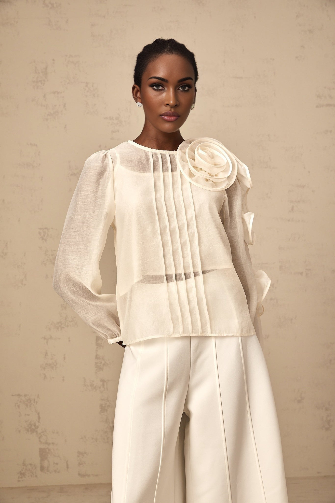 A lightcolored blouse with delicate threedimensional flower details and semisheer fabric