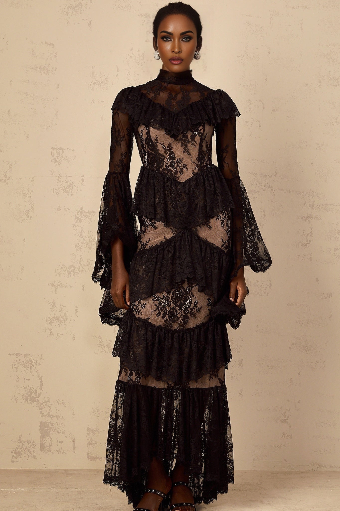 A long black maxi dress with floral lace details and ruffled accents worn by a model against a plain background