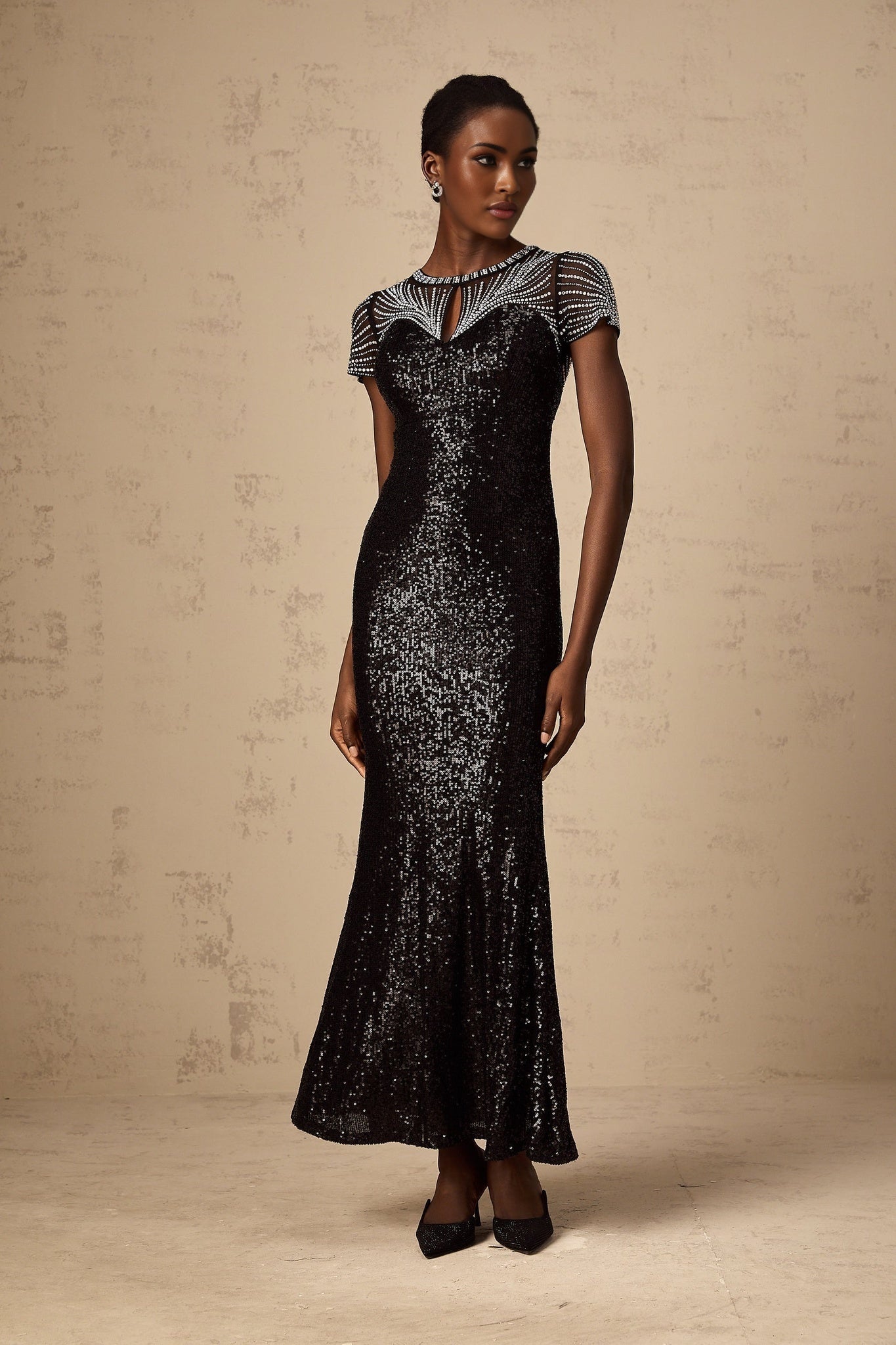 A long black maxi dress with sequin embellishments and cutout details worn by a model against a plain background