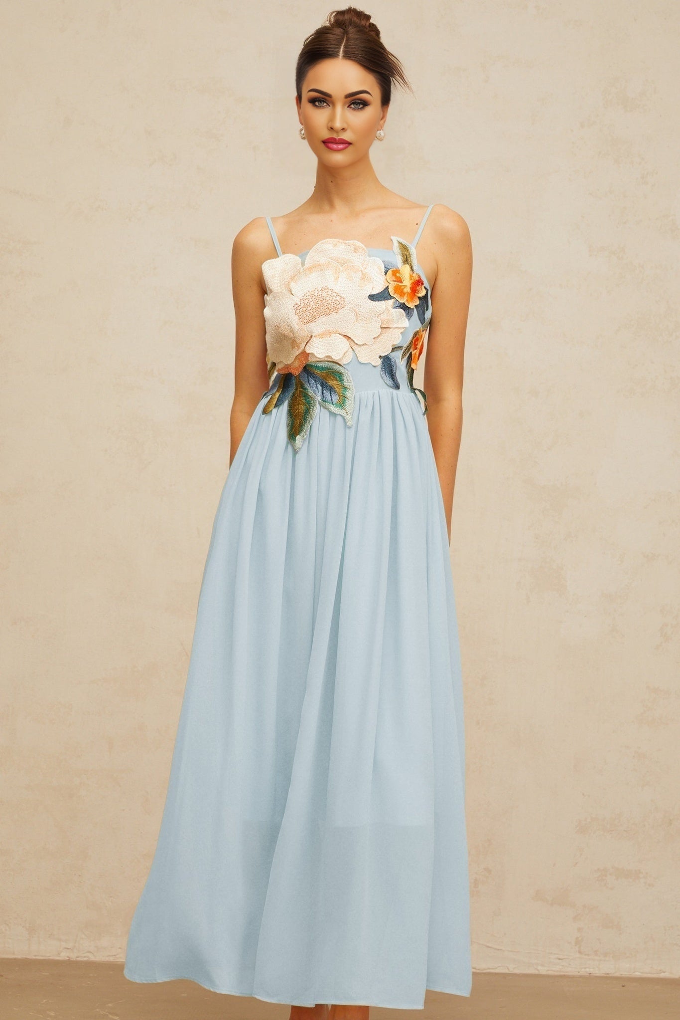 A long blue maxi dress with shirred detailing and floral embroidery covering the fabric named Josette