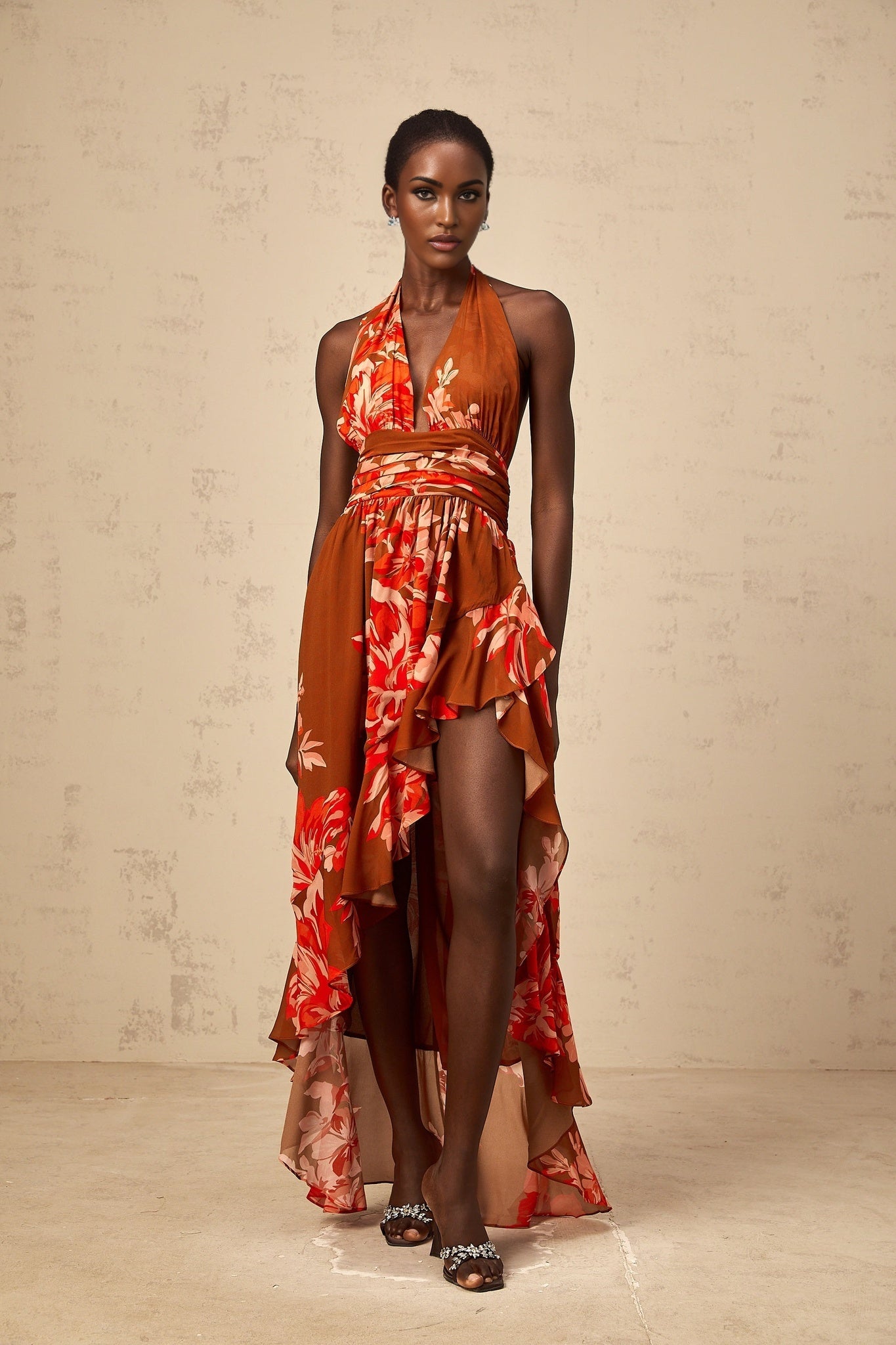 A long brown dress with a floral print pattern featuring an asymmetrical hemline and a flowing maxi silhouette