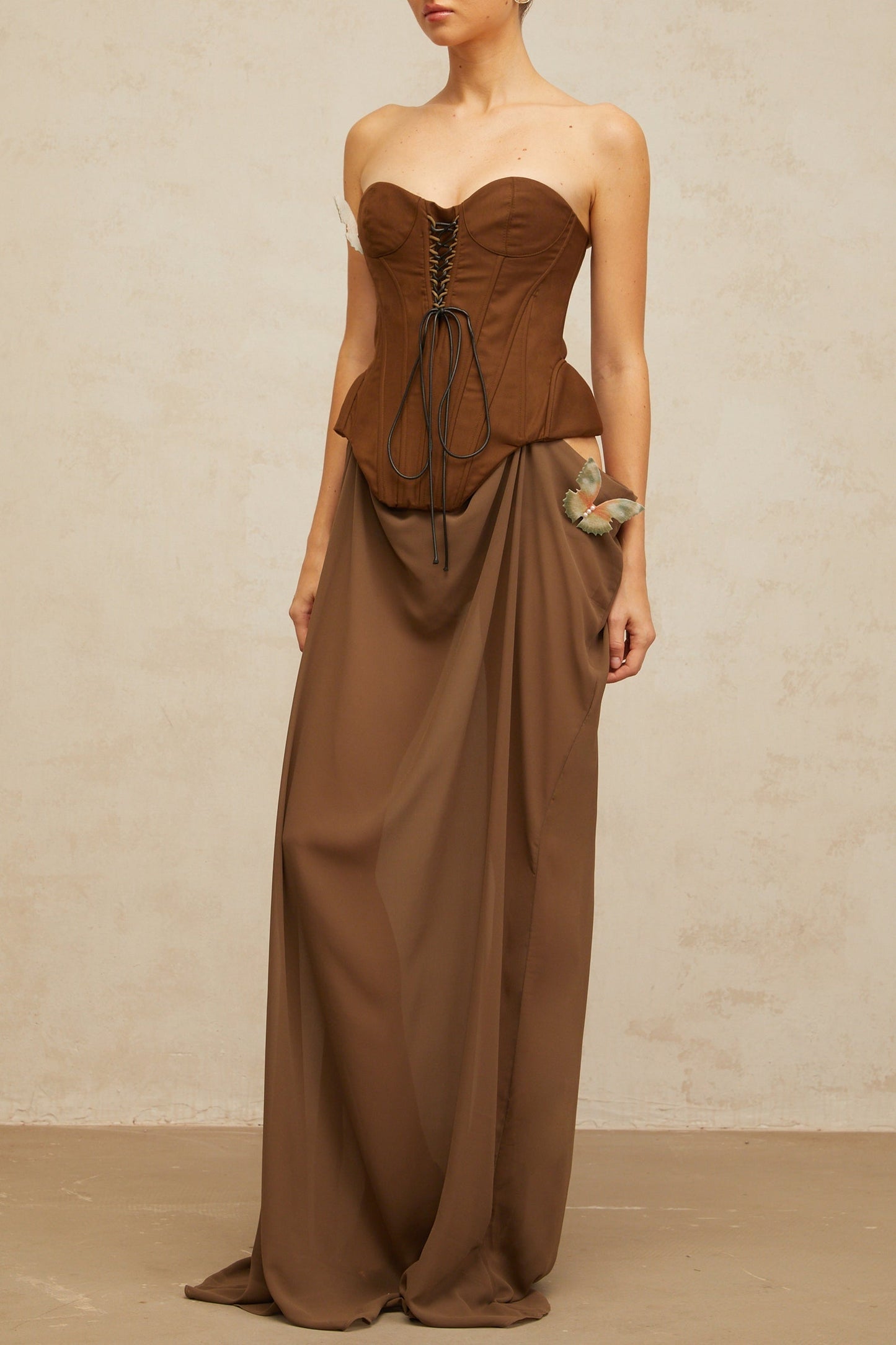 A long brown maxi dress with a corsetstyle bodice featuring butterfly pin details and a flowing skirt