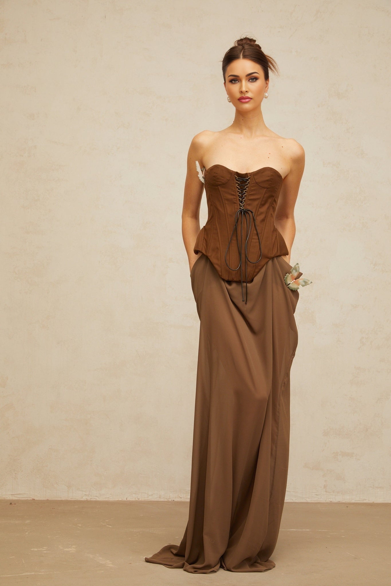 A long brown maxi dress with a corsetstyle bodice featuring butterfly shaped pin details and a flowing skirt