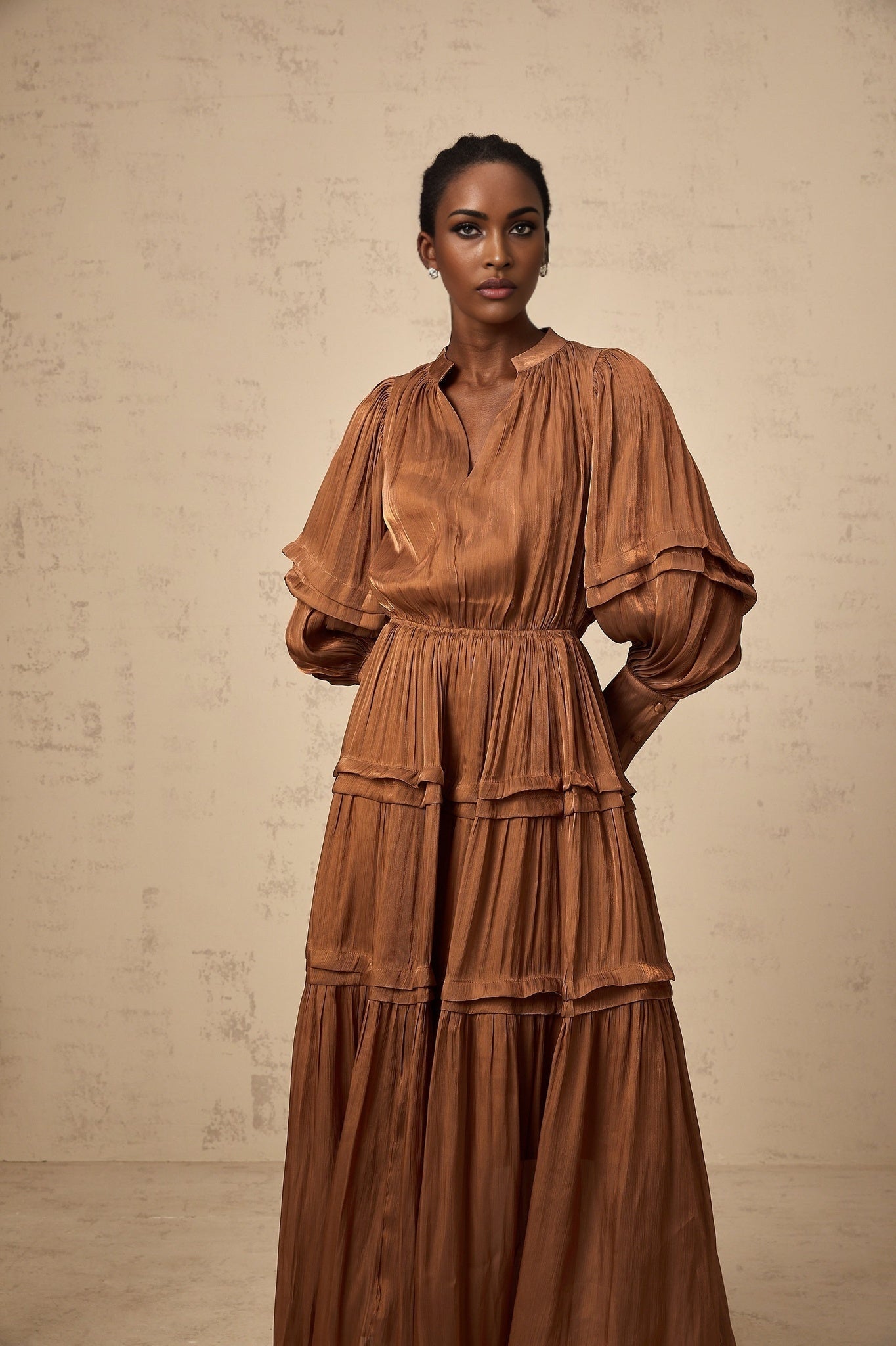 A long brown maxi dress with ruffled trim and tiered layers worn by a model