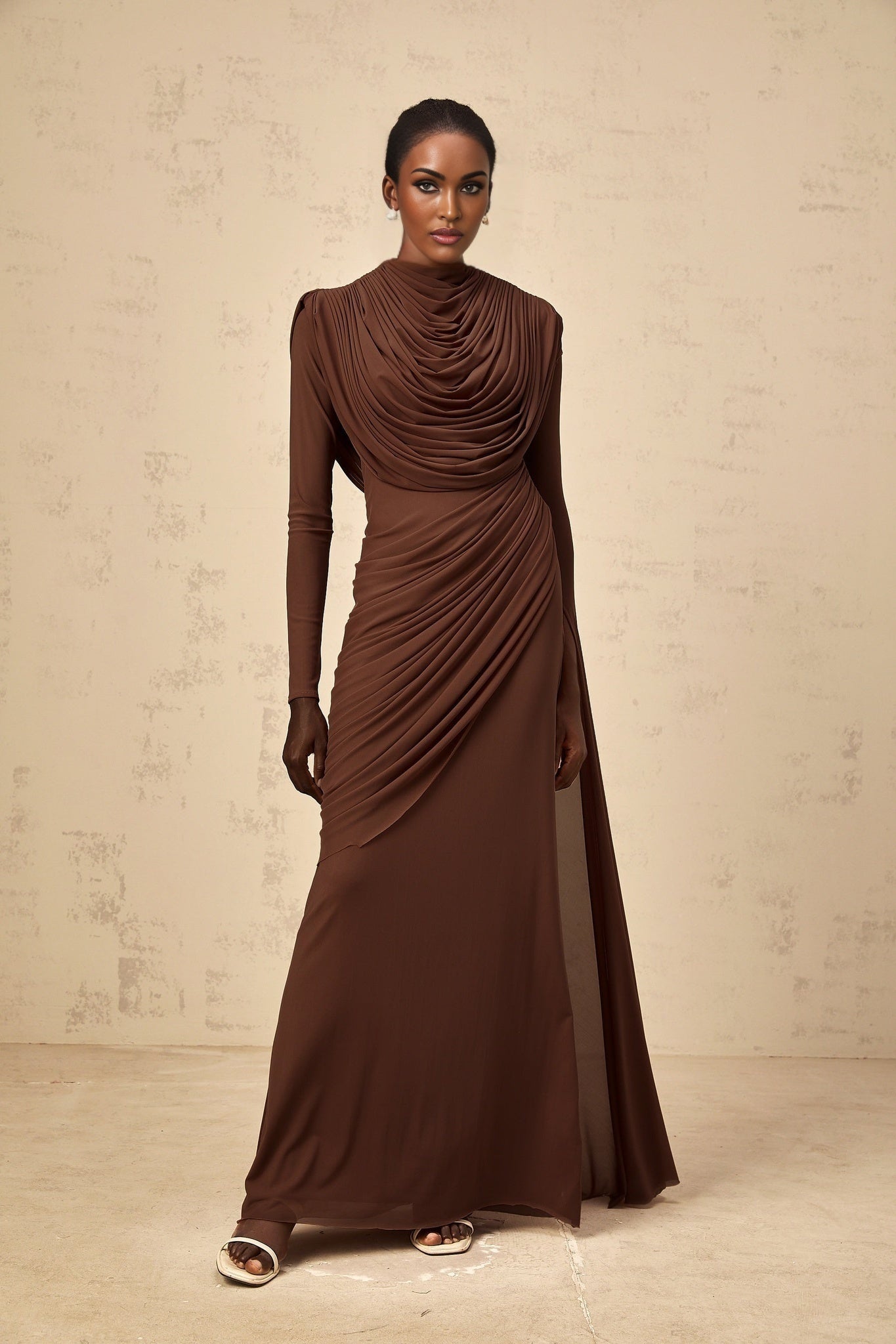 A long brown maxi dress with shirred detailing and draped fabric flowing to the floor
