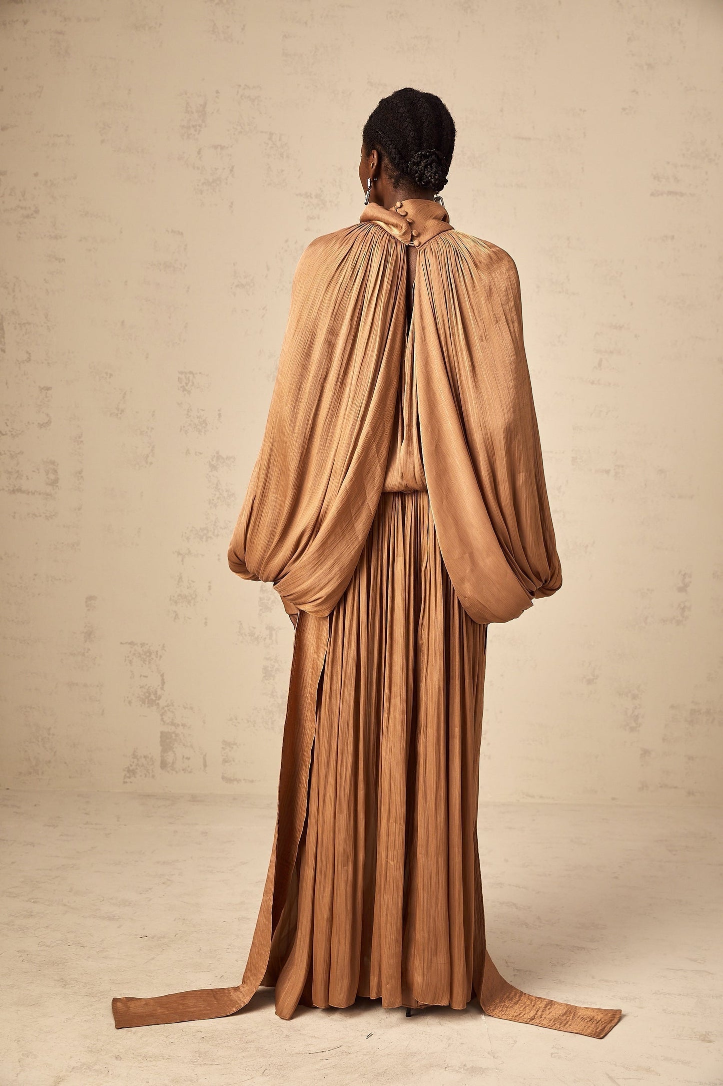 A long brown pleated satin maxi dress with a flowing silhouette and elegant drape