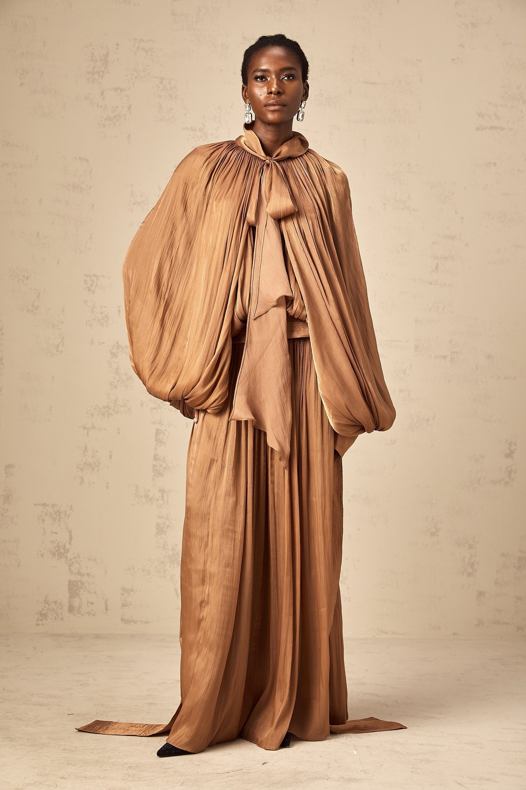 A long brown pleated satin maxi dress with a flowing silhouette and shiny fabric