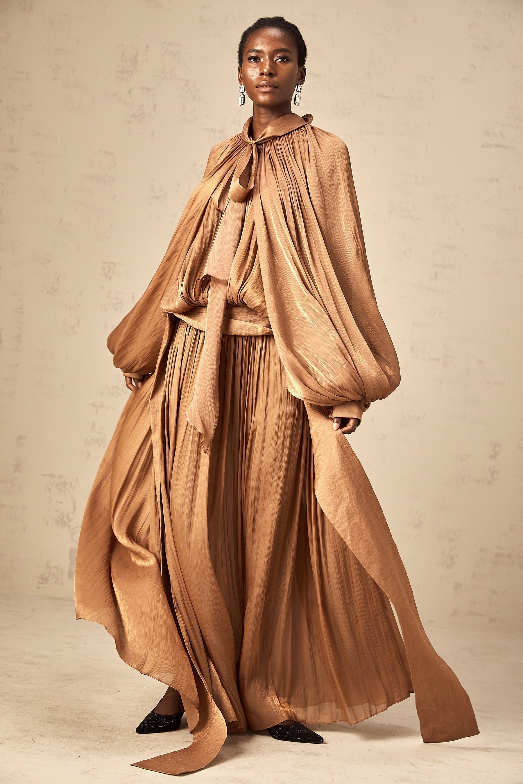 A long brown pleated satin maxi dress with a flowing silhouette