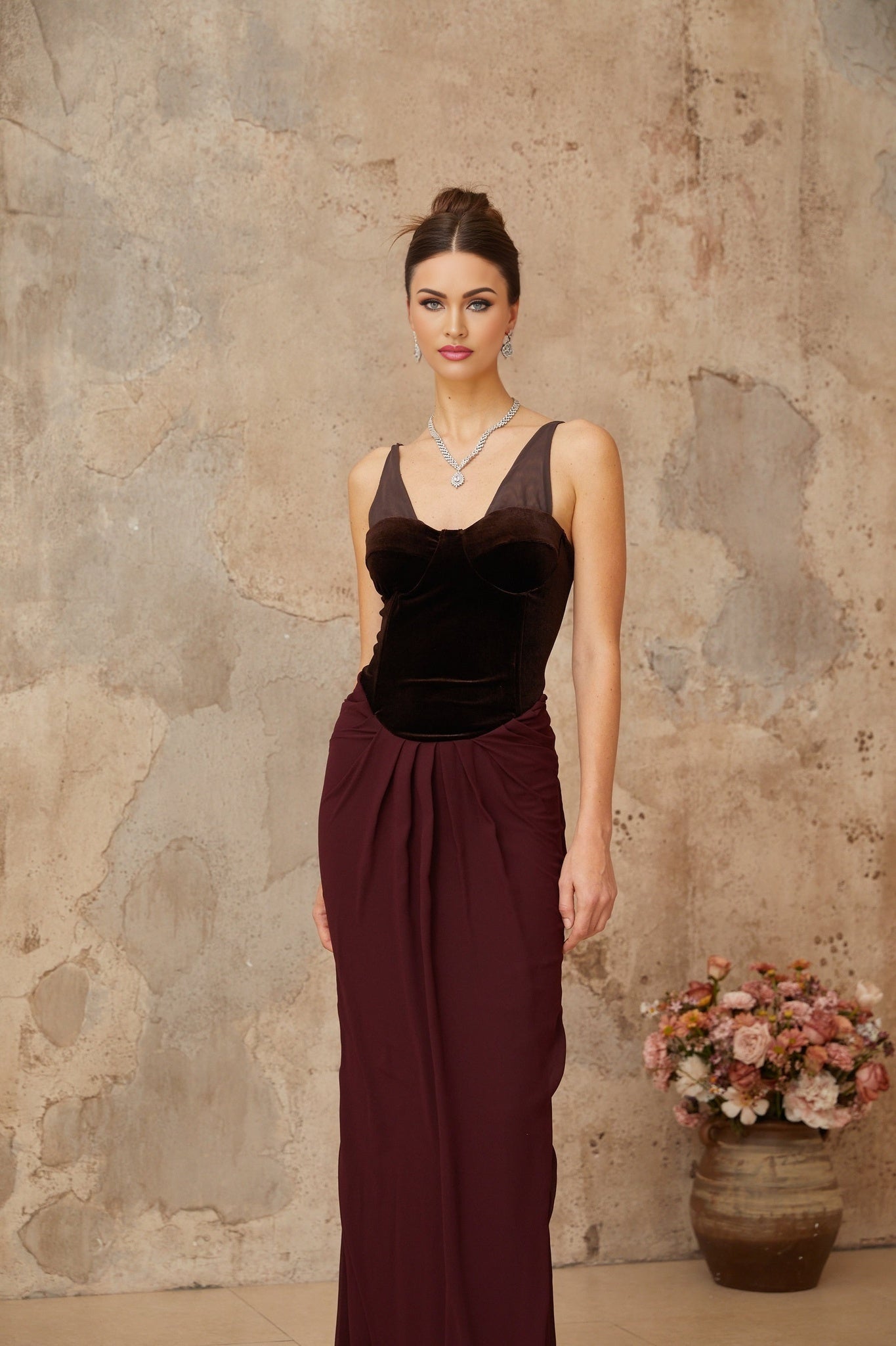 A long burgundy maxi dress with velvet panels and shirred detailing featuring a flowing silhouette and elegant design
