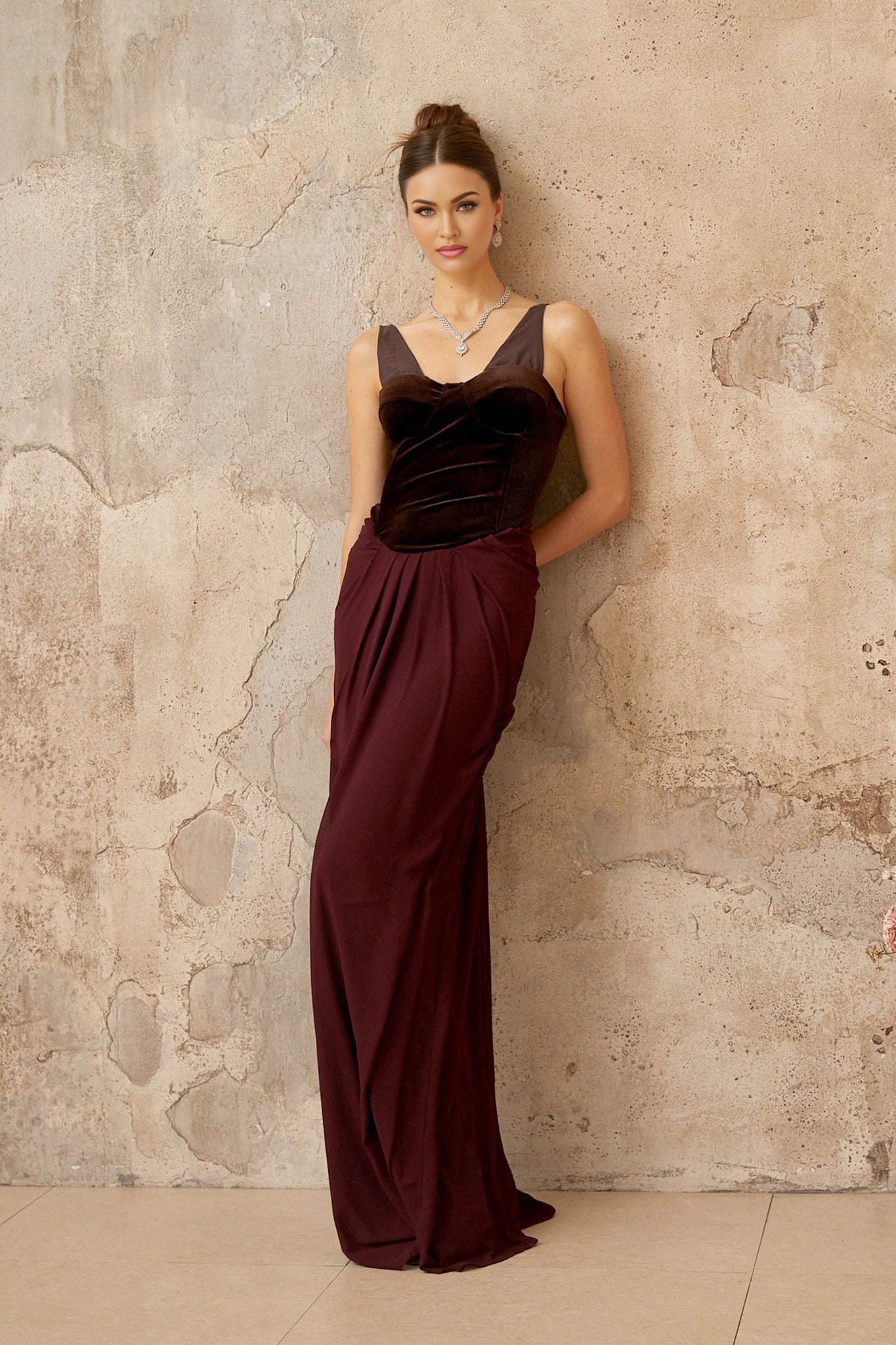 A long burgundy maxi dress with velvet panels and shirred detailing featuring a flowing silhouette and elegant design