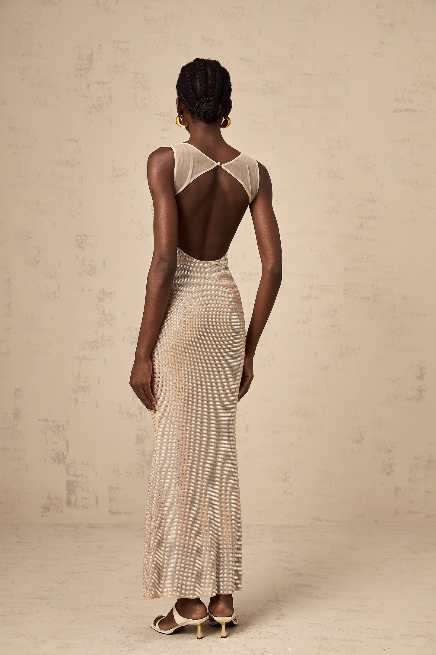 A long elegant maxi dress with crystal embellishments and an open back design featuring a flowy silhouette in a light color