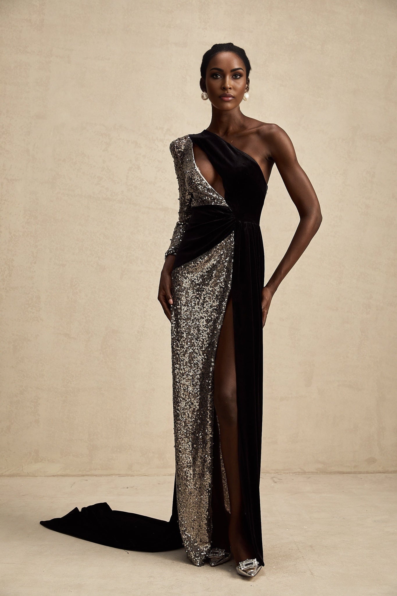 A long flowing asymmetric maxi dress covered in shimmering sequins featuring a oneshoulder design and a high slit