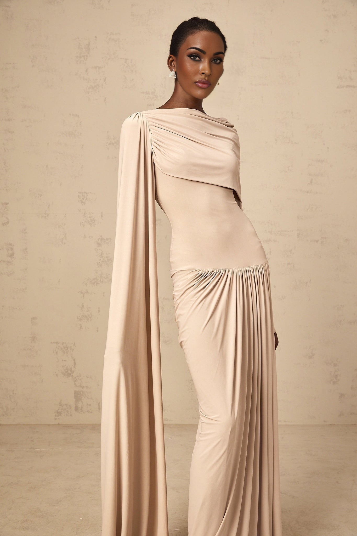 A long flowing maxi dress in neutral tones featuring a ribbon design and draped silhouette