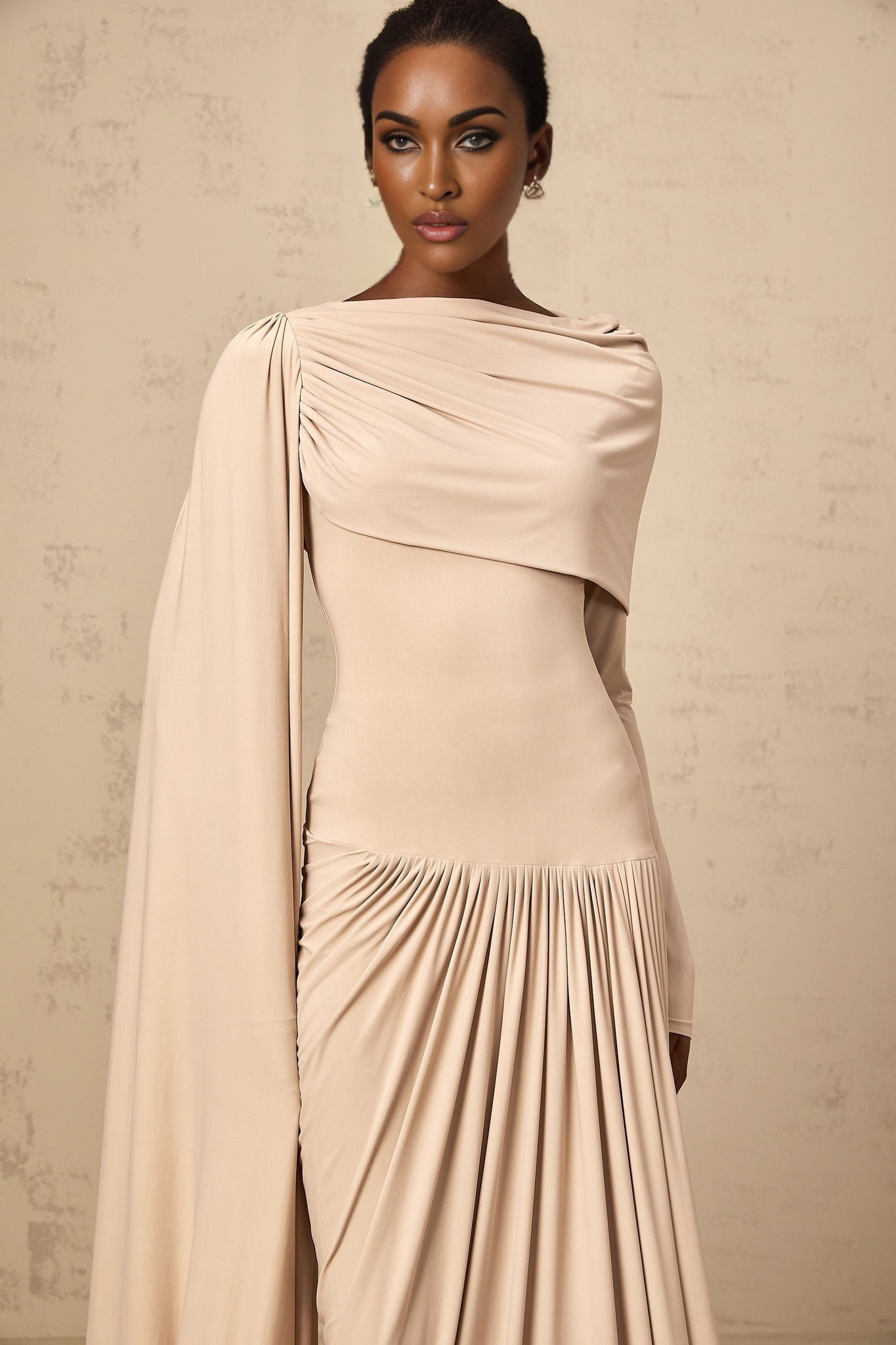 A long flowing maxi dress in neutral tones featuring draped fabric and ribbon design details