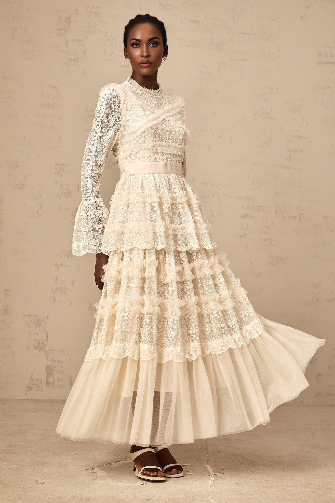 A long flowy maxi dress in neutral tones with lace panels and ruffle details made from tulle fabric