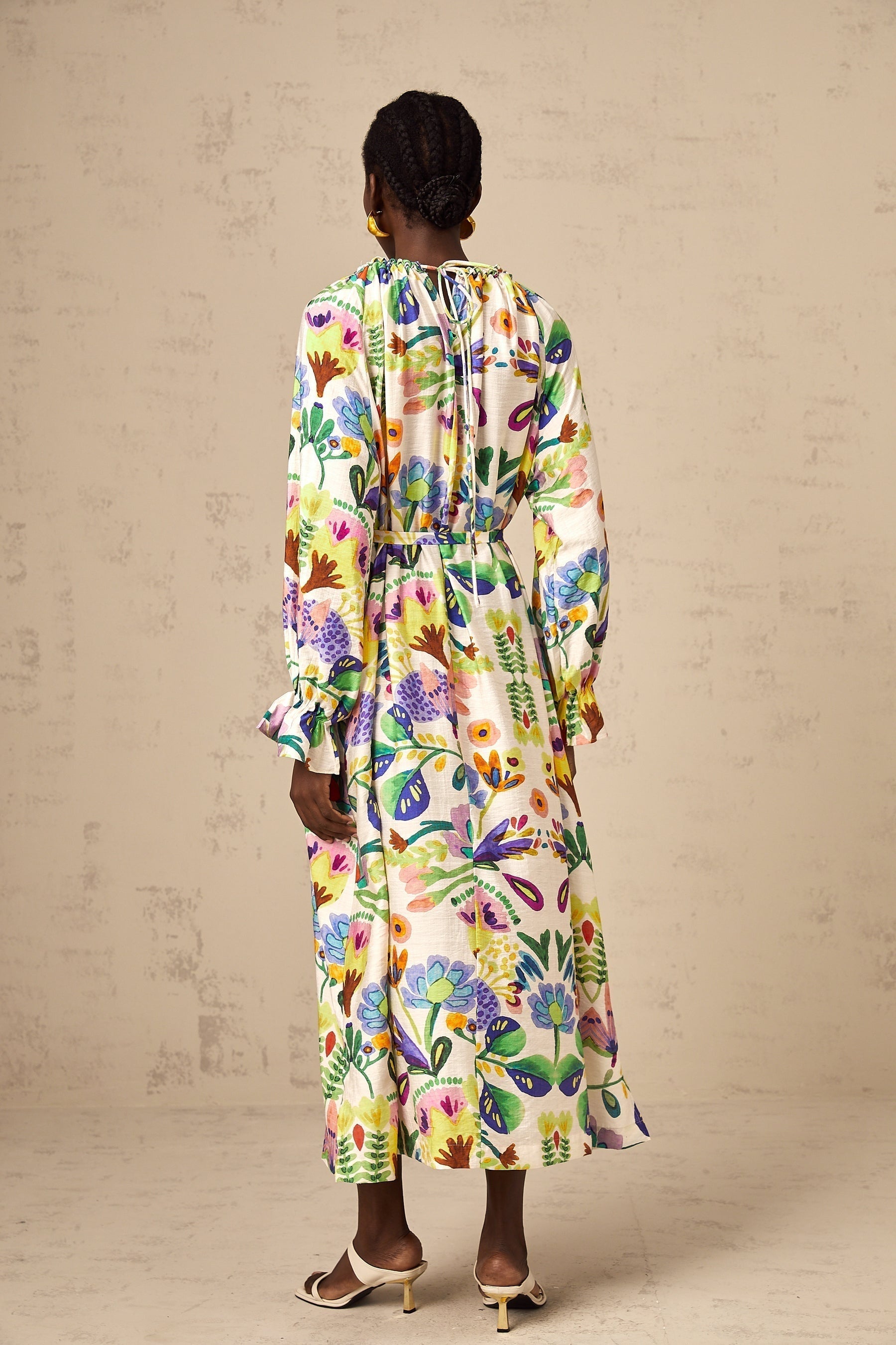 A long flowy midi dress with a colorful paisley print pattern on white poplin fabric featuring a feminine silhouette and lightweight airy design