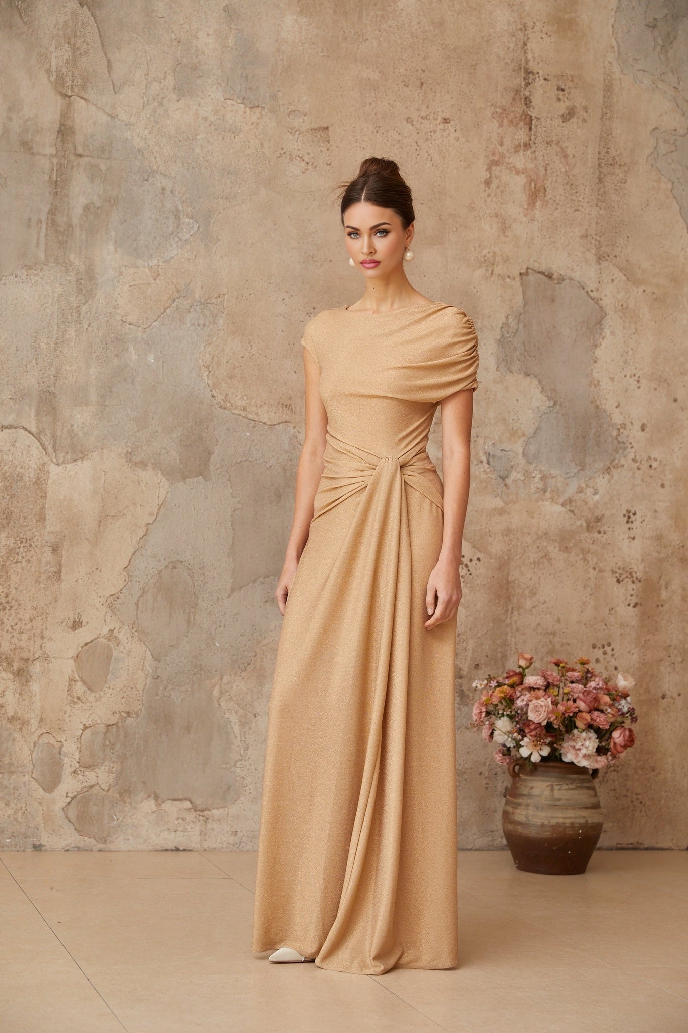 A long gold maxi dress with an asymmetrical neckline and pleated skirt flowing elegantly to the floor