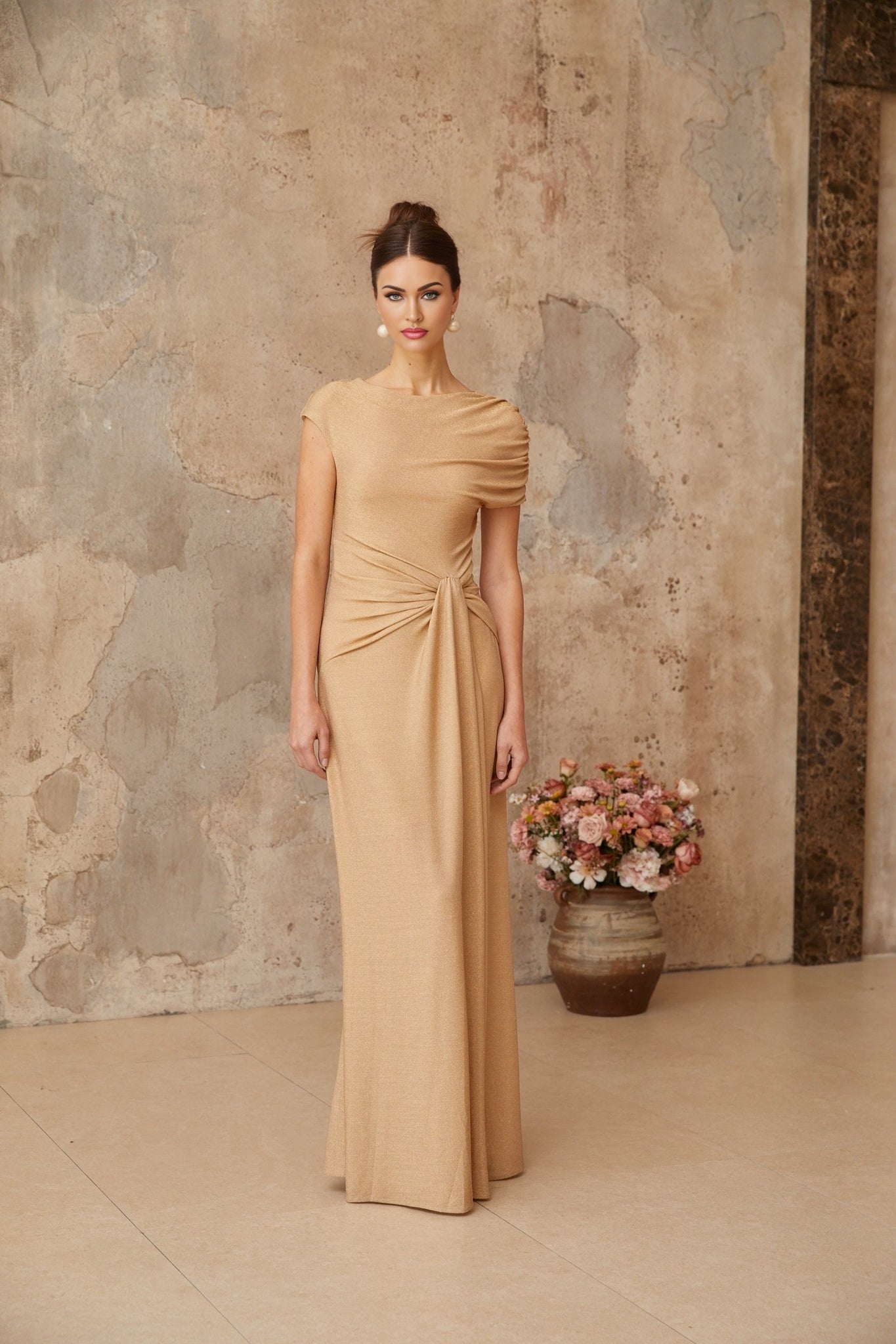A long gold maxi dress with an asymmetrical pleated design and a flowing silhouette named Rosalie