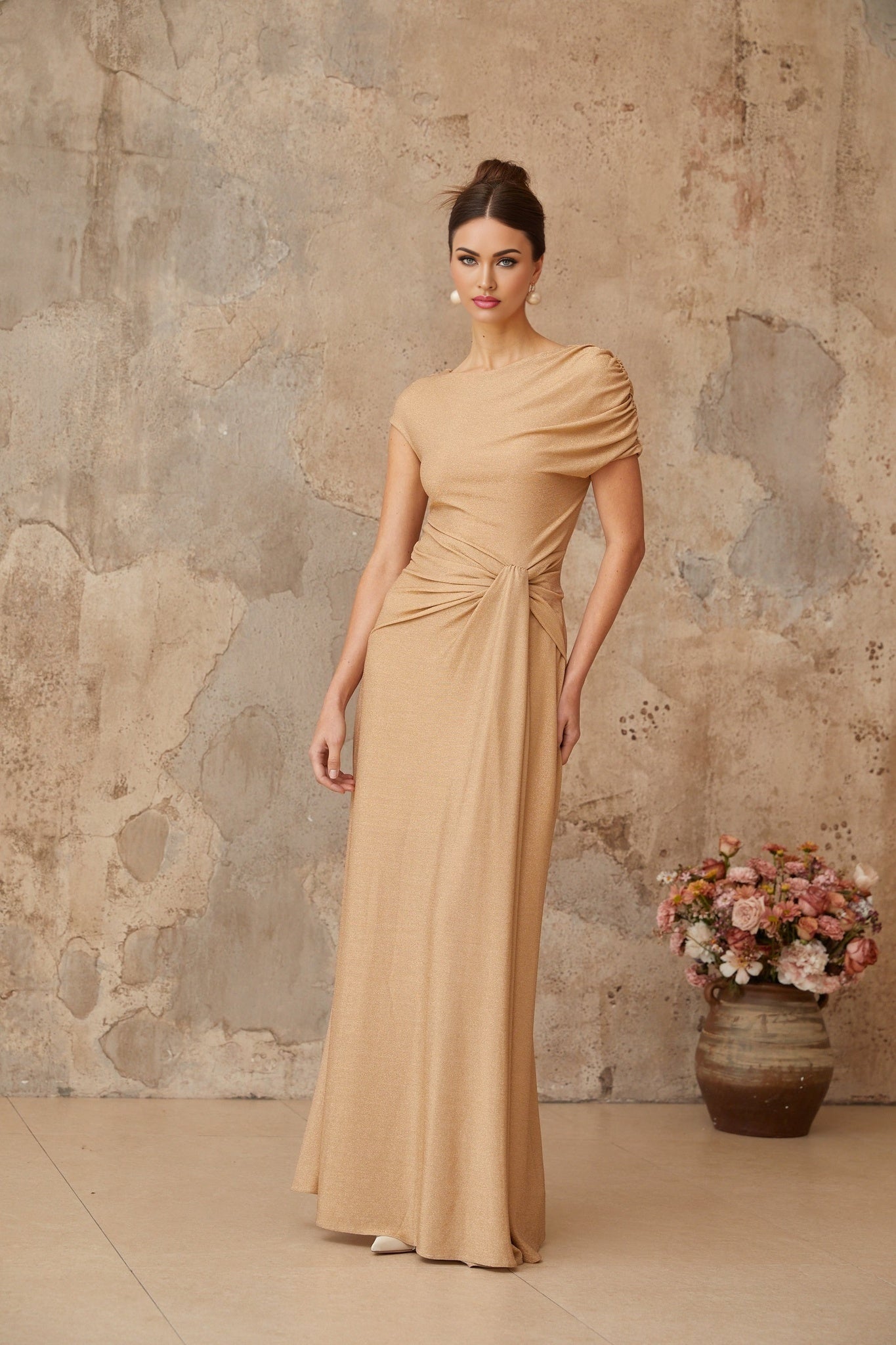 A long gold maxi dress with an asymmetrical pleated design and a flowing silhouette named Rosalie