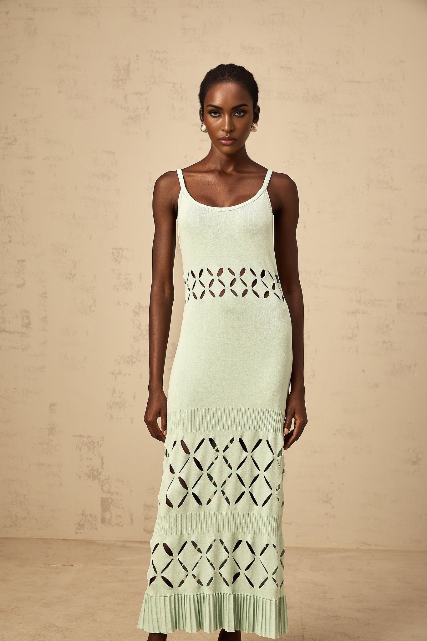 A long green knitted maxi dress with cut out details worn by a model standing against a plain background