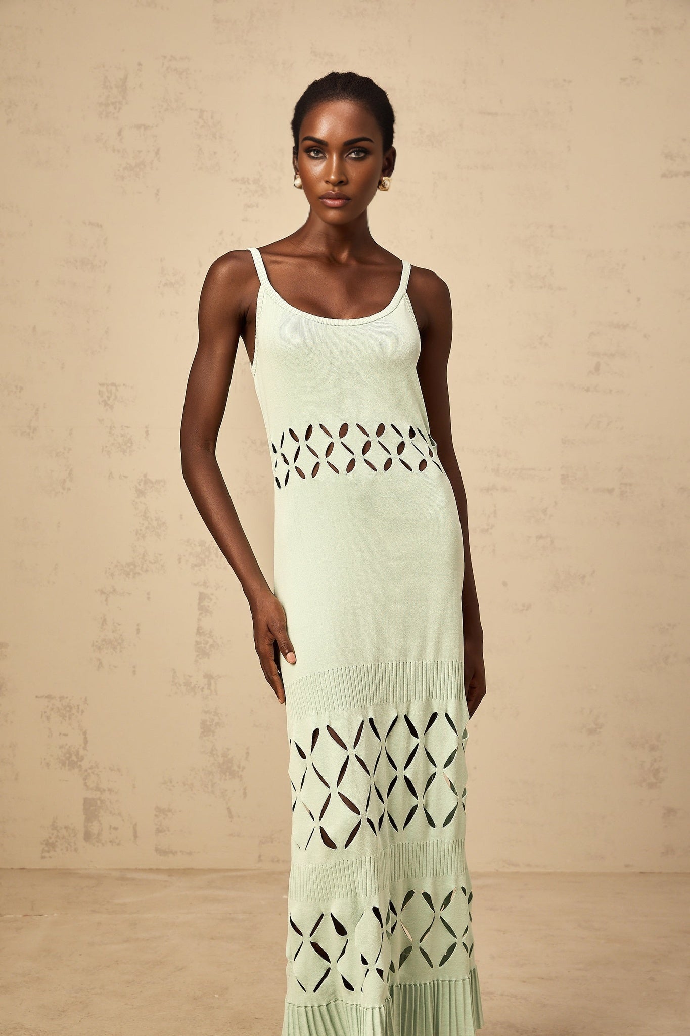 A long green knitted maxi dress with cutout details featuring a formfitting silhouette and sleeveless design