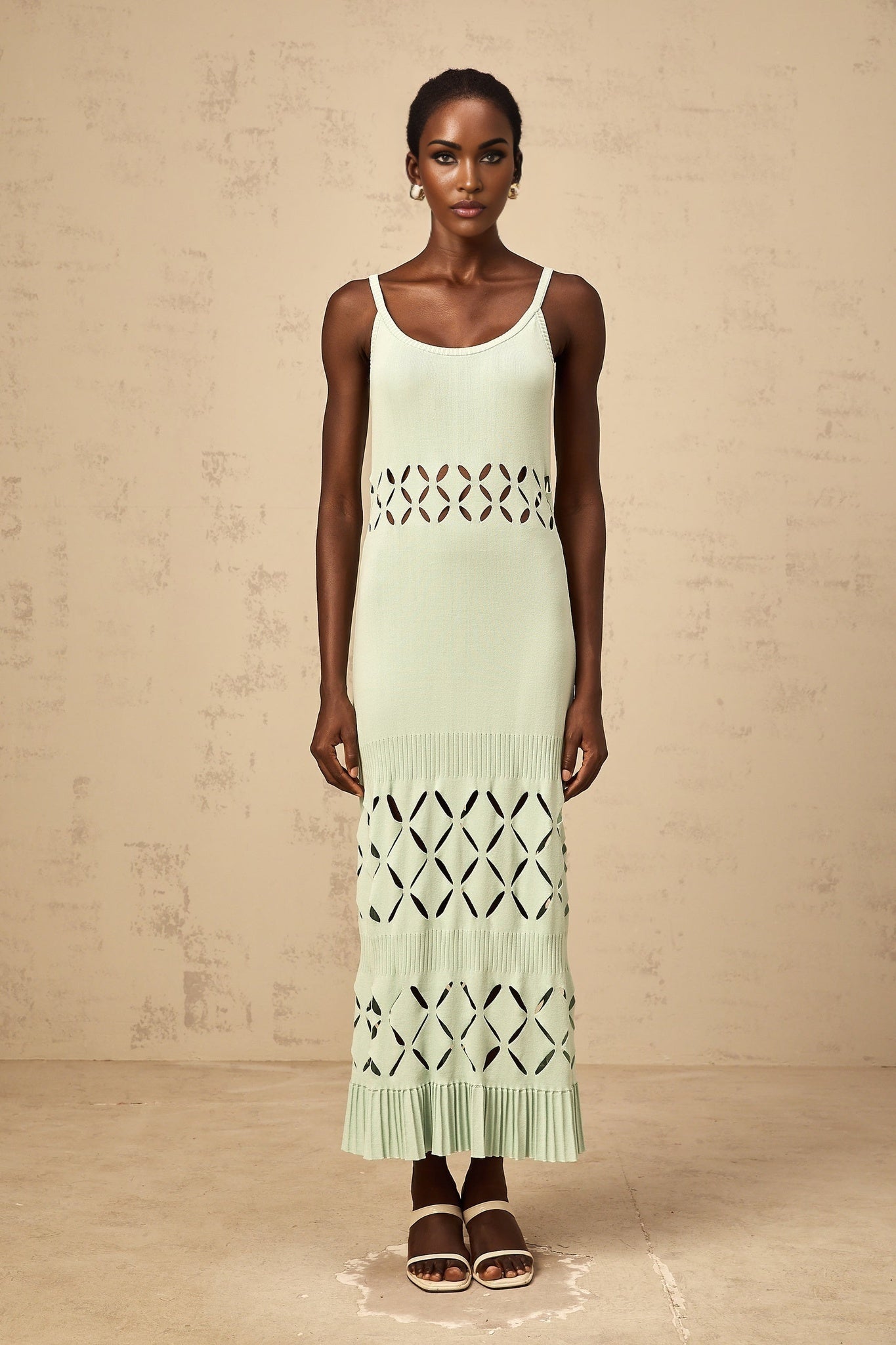 A long green knitted maxi dress with cutout details worn by a model standing against a plain background