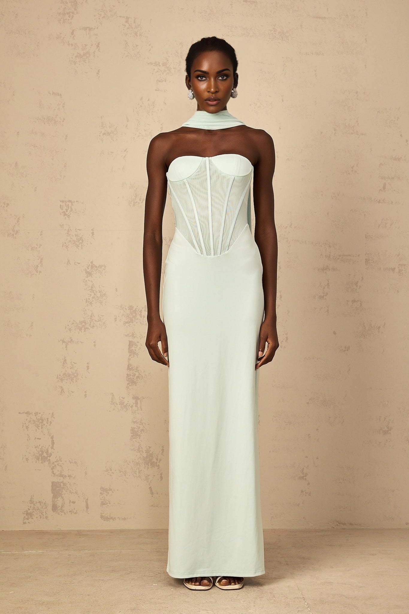 A long mint green maxi dress with a tulle panel and corset bodice featuring a flowy skirt and delicate sheer details