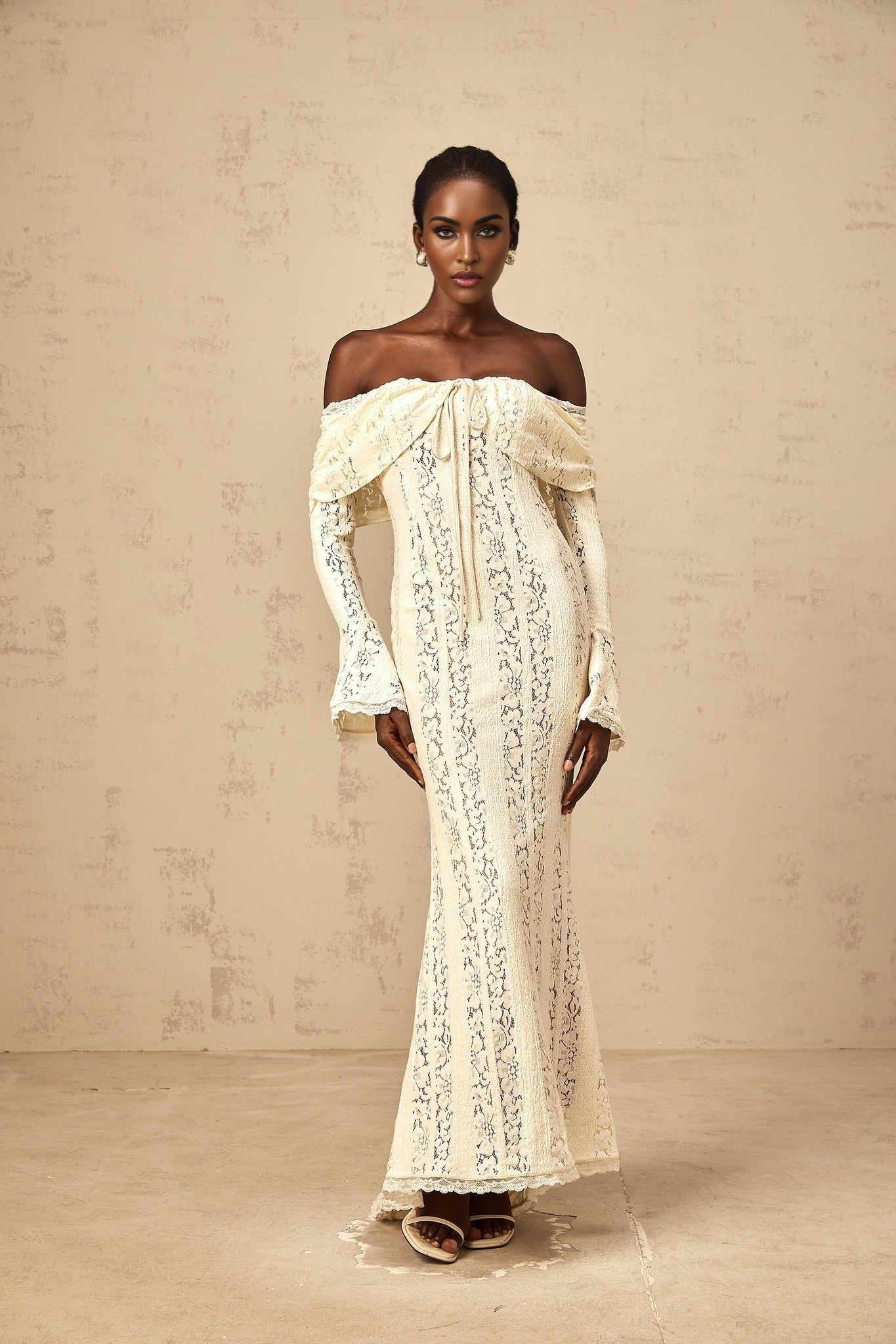 A long neutral colored maxi dress with floral lace detailing and a train design featuring delicate patterns and a flowing silhouette