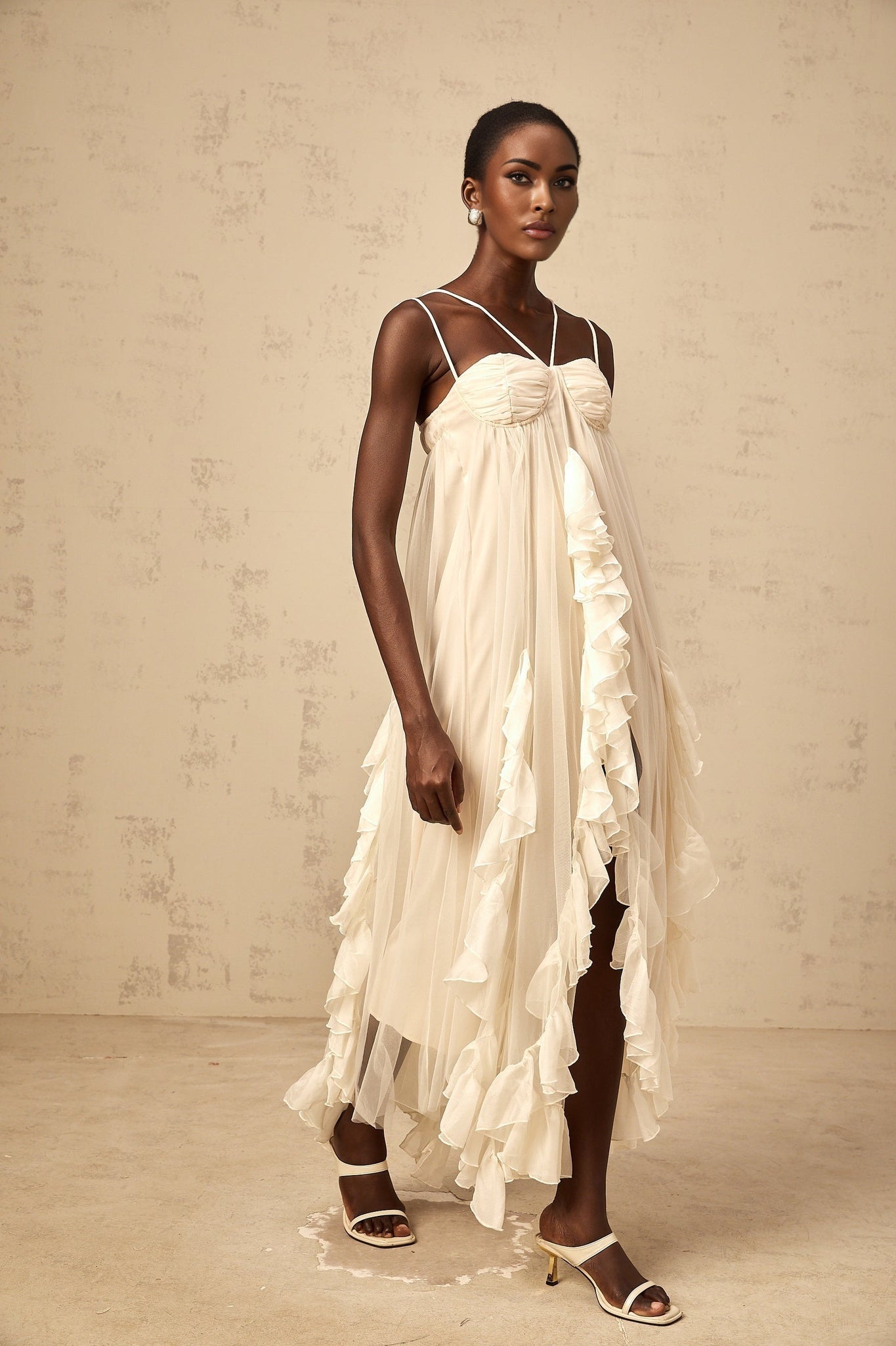 A long neutralcolored maxi dress with multiple layers of ruffled tulle creating a flowing and ethereal appearance
