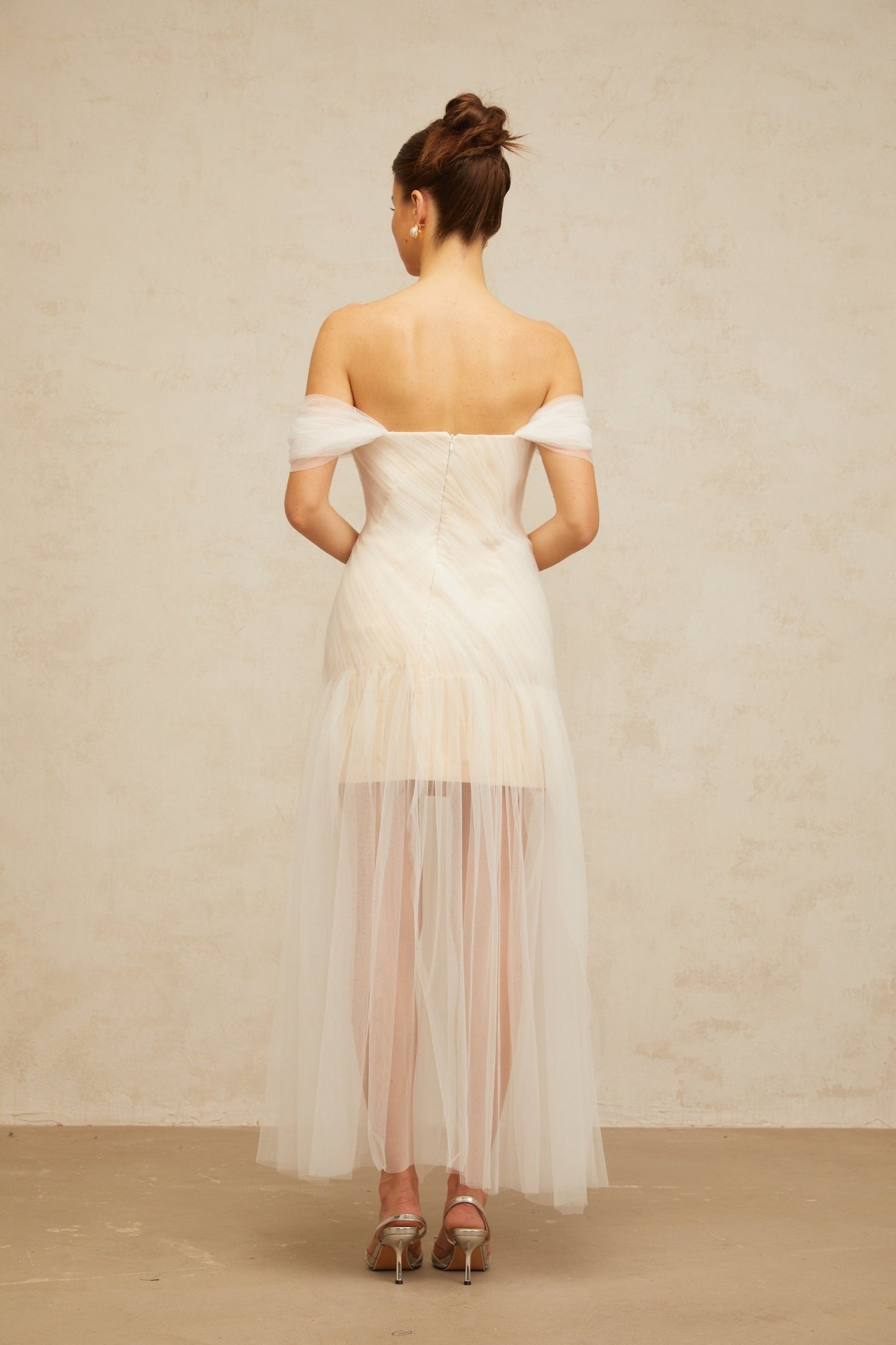 A long off white maxi dress with pleated tulle fabric and flowy silhouette worn by a model standing in a neutral background