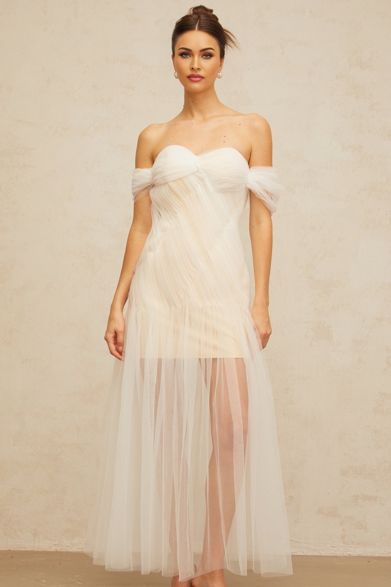 A long off white maxi dress with pleated tulle fabric featuring a flowy silhouette and delicate design details