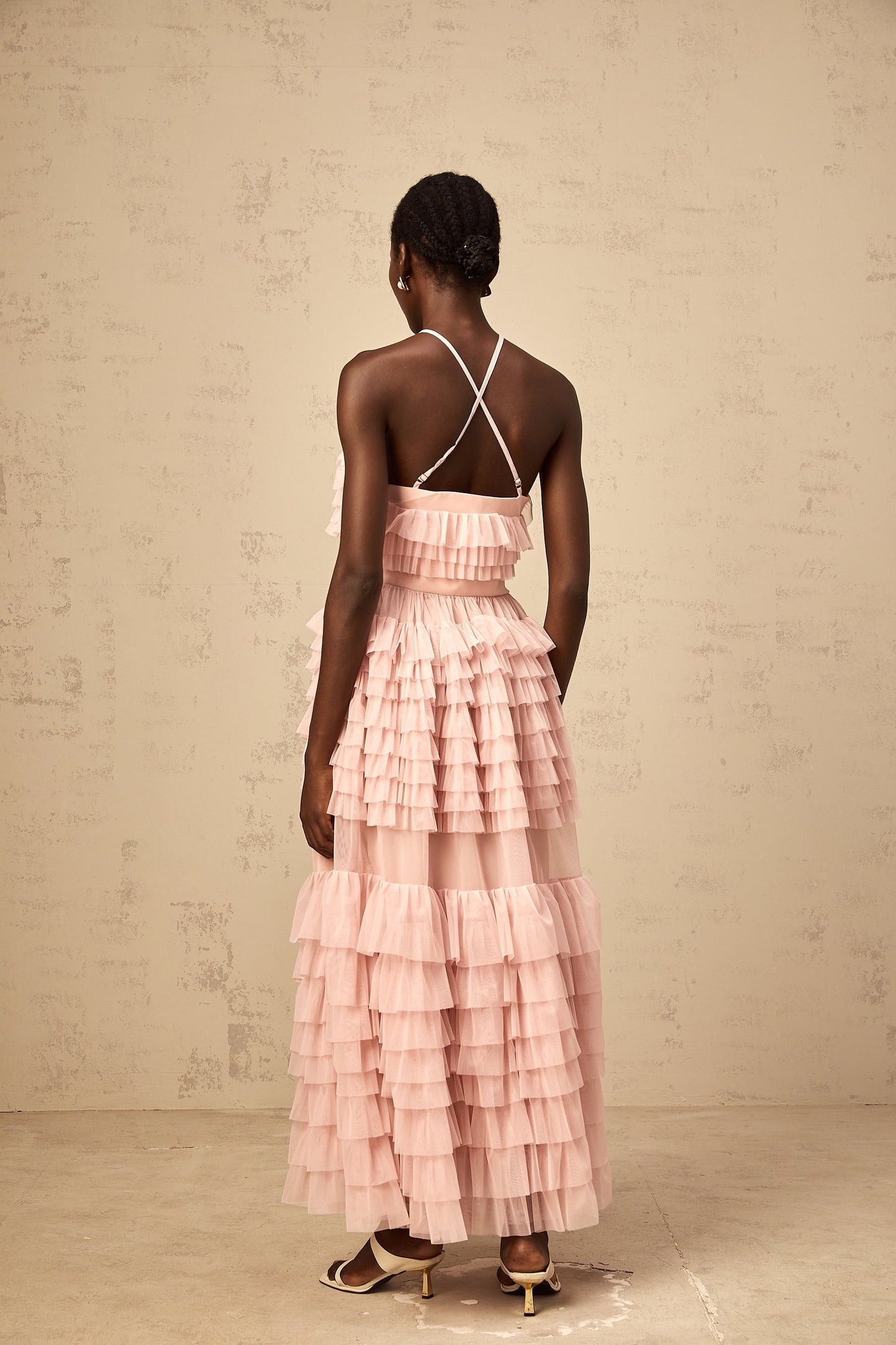 A long pink maxi dress with a tiered tulle skirt and ruffled details featuring a floral petal brooch at the waist named Isabelle