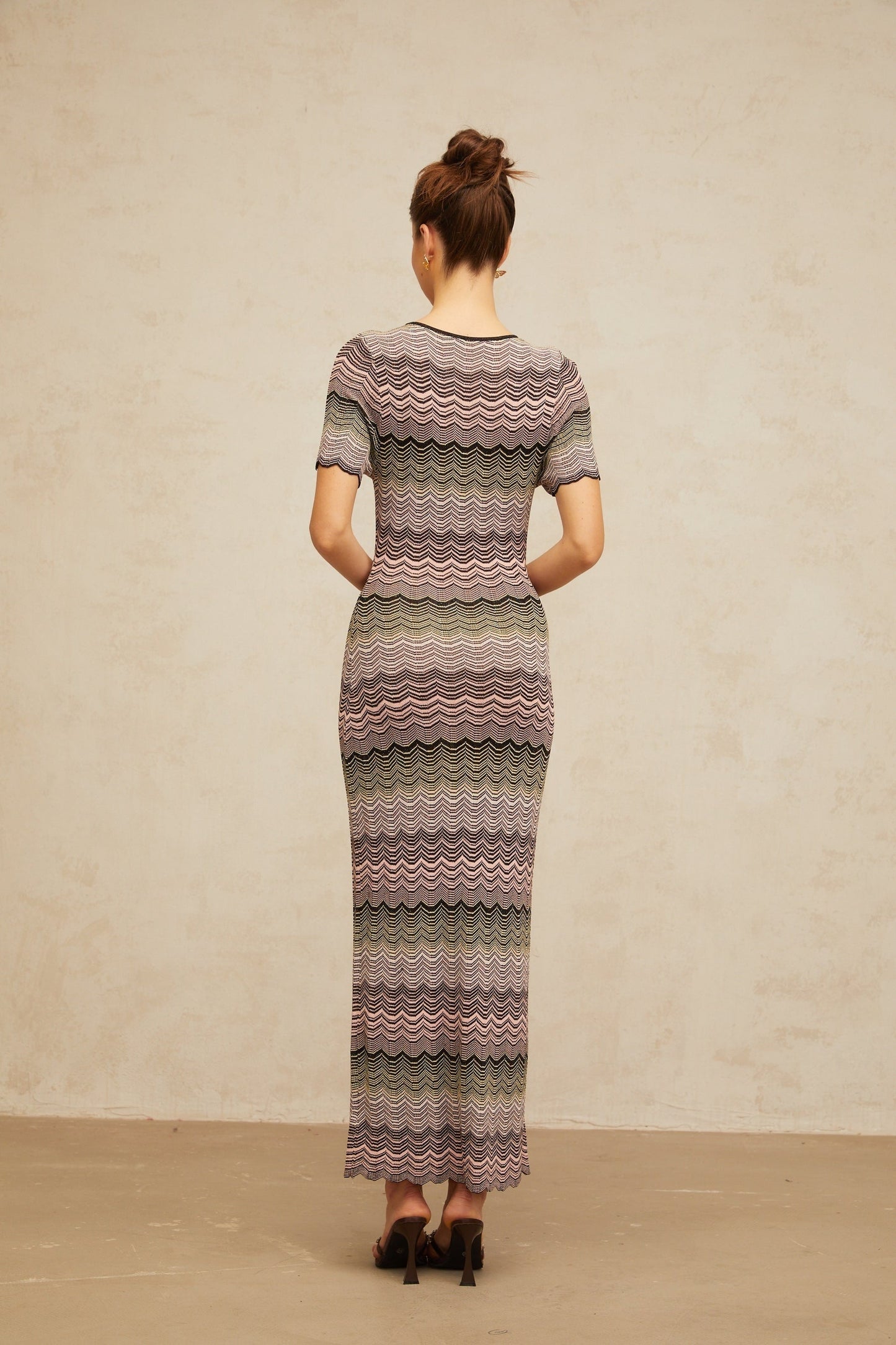 A long pink maxi dress with a wavy crochet knit pattern throughout featuring a fitted bodice and flowing skirt