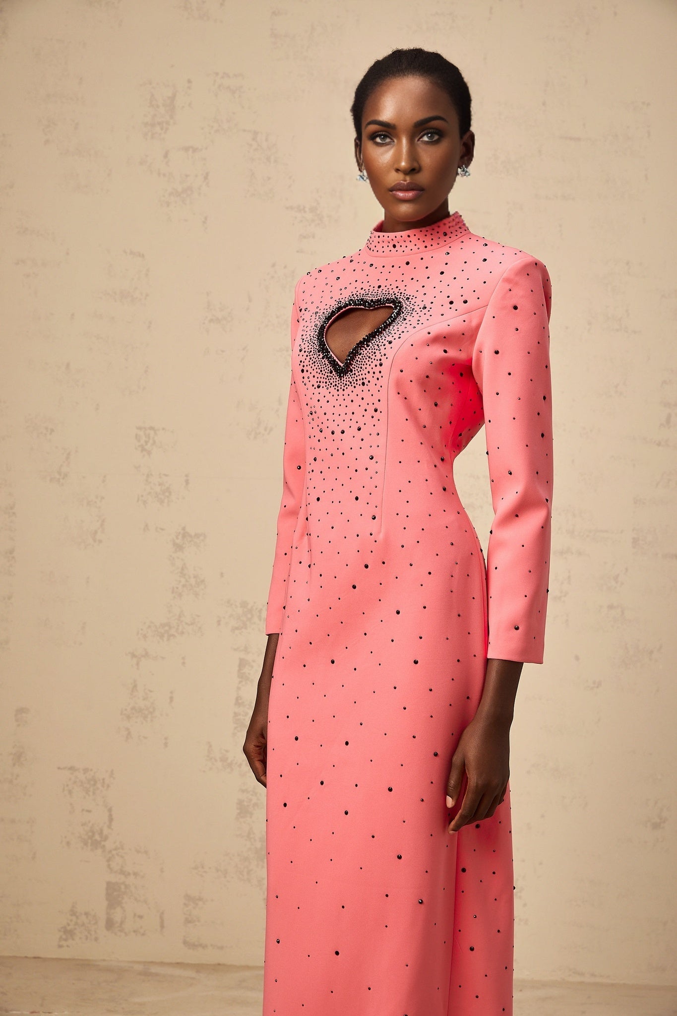 A long pink maxi dress with heart shaped cutouts and embellishments featuring a flowy silhouette and romantic design