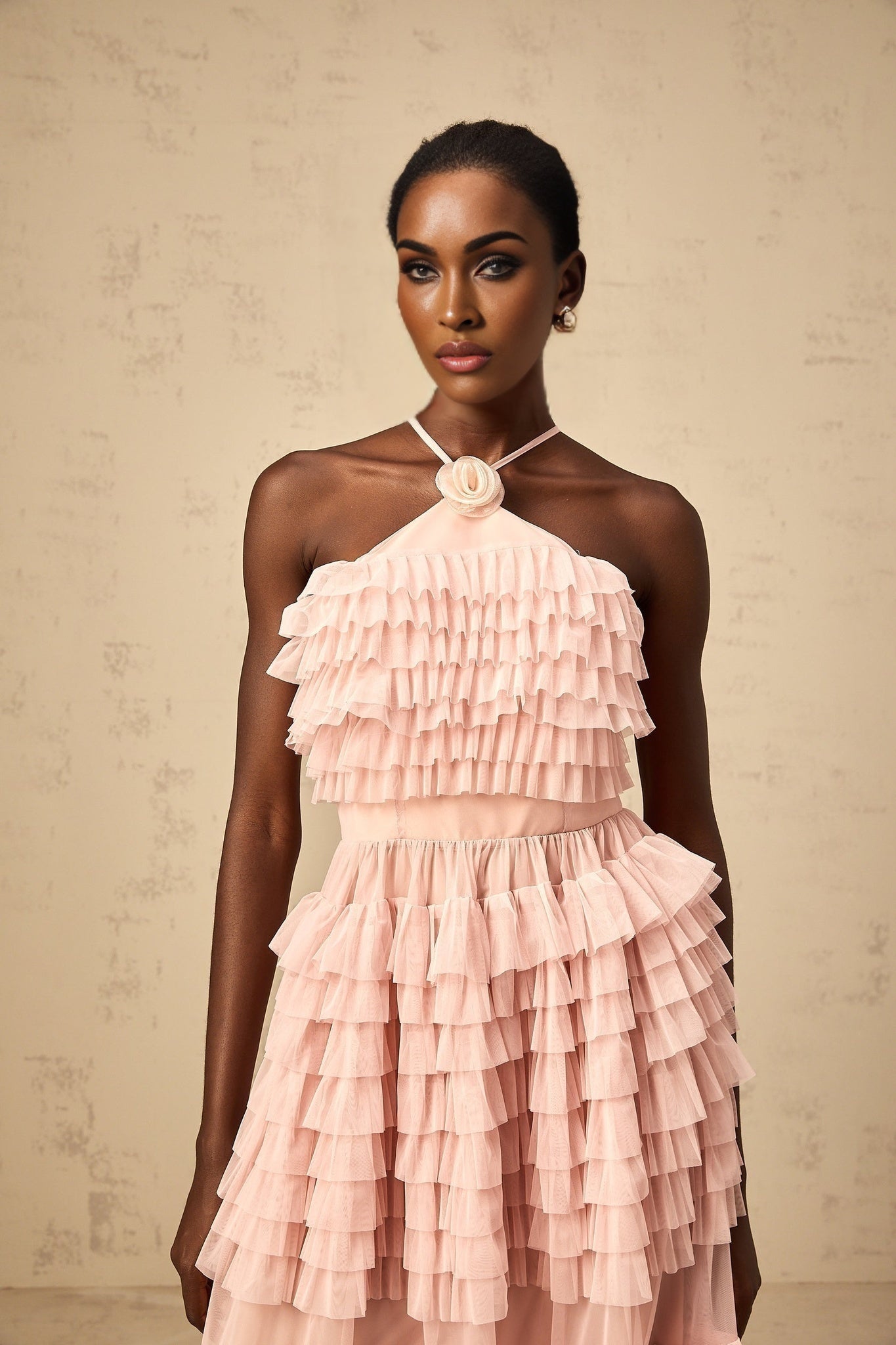 A long pink maxi dress with tiered ruffles and a tulle skirt featuring a petal shaped brooch at the waist