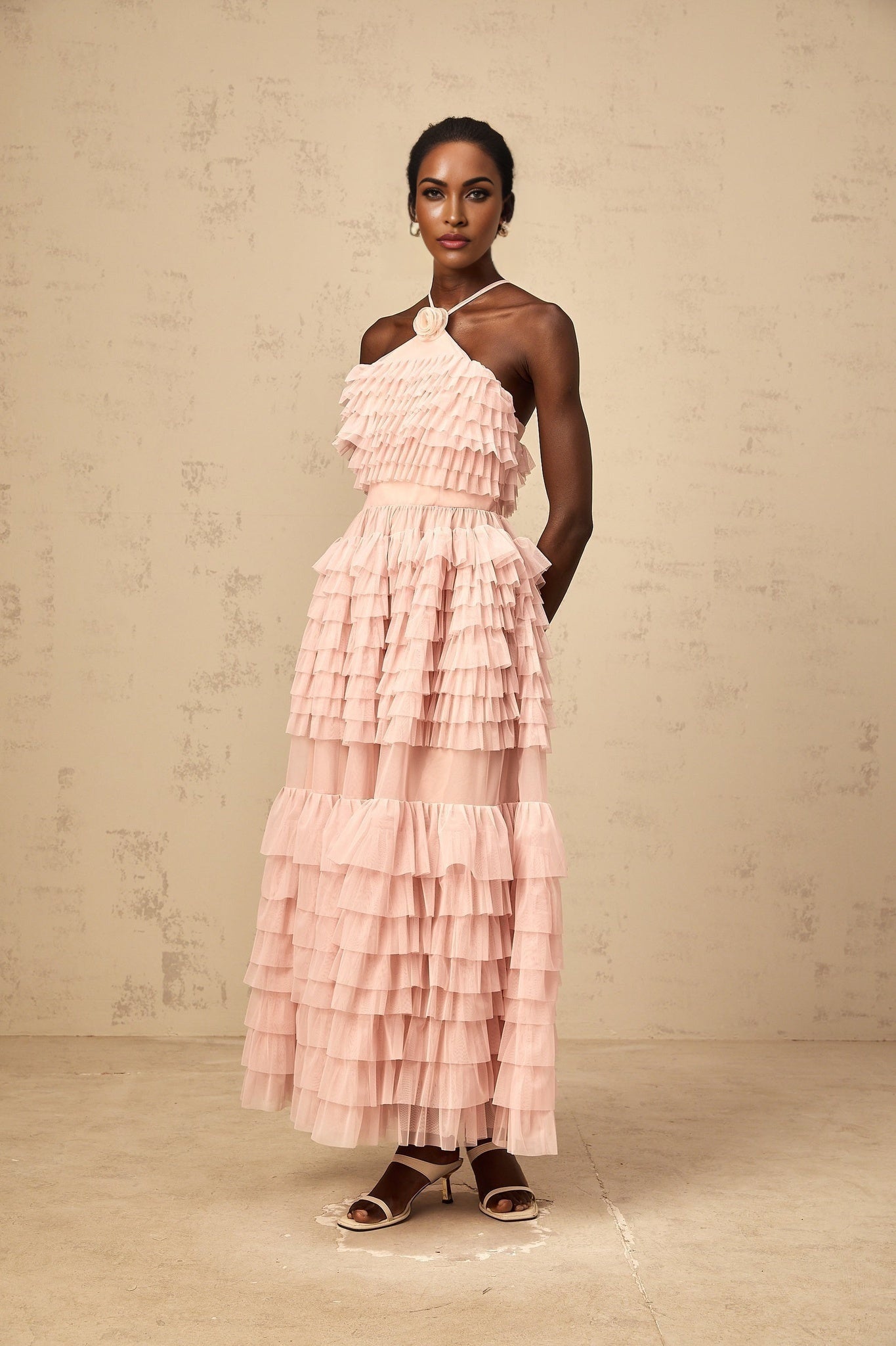 A long pink tiered tulle maxi dress with ruffles and a floral brooch accent at the waist