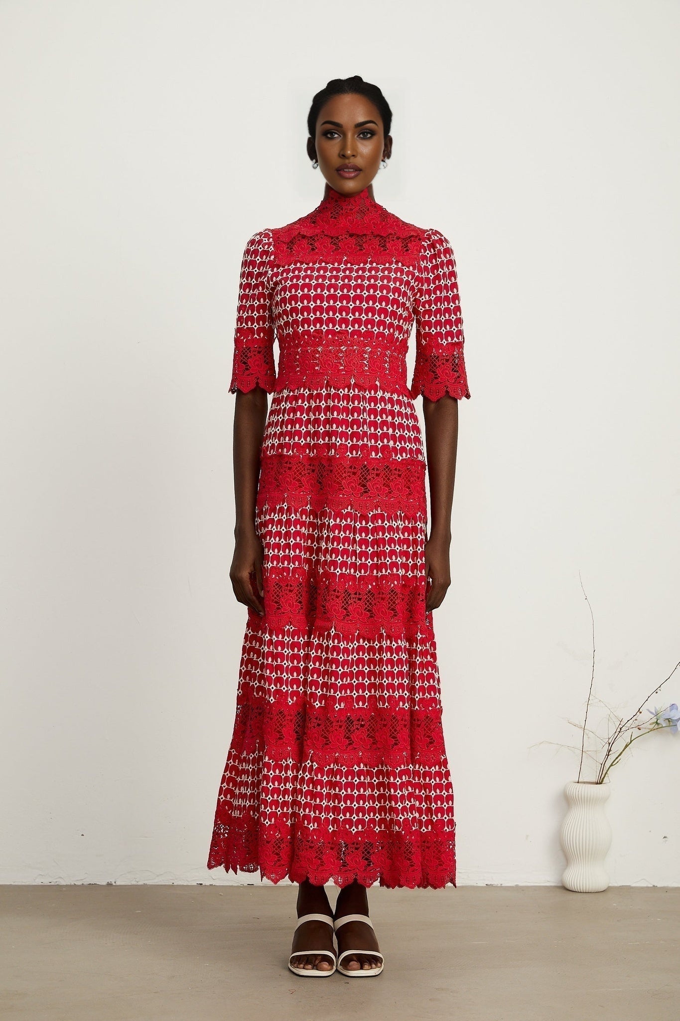 A long red maxi dress with scalloped lace panels featuring a delicate pattern throughout the garment