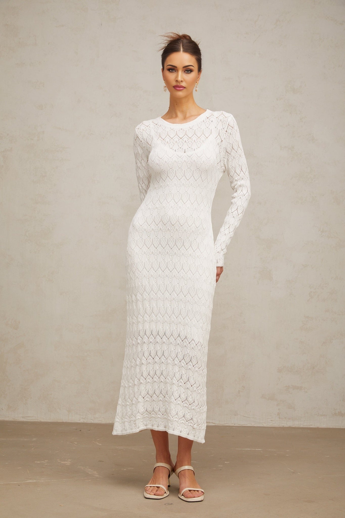A long white dress with crochet knit pattern and midi length featuring a sleeveless design and intricate lace details